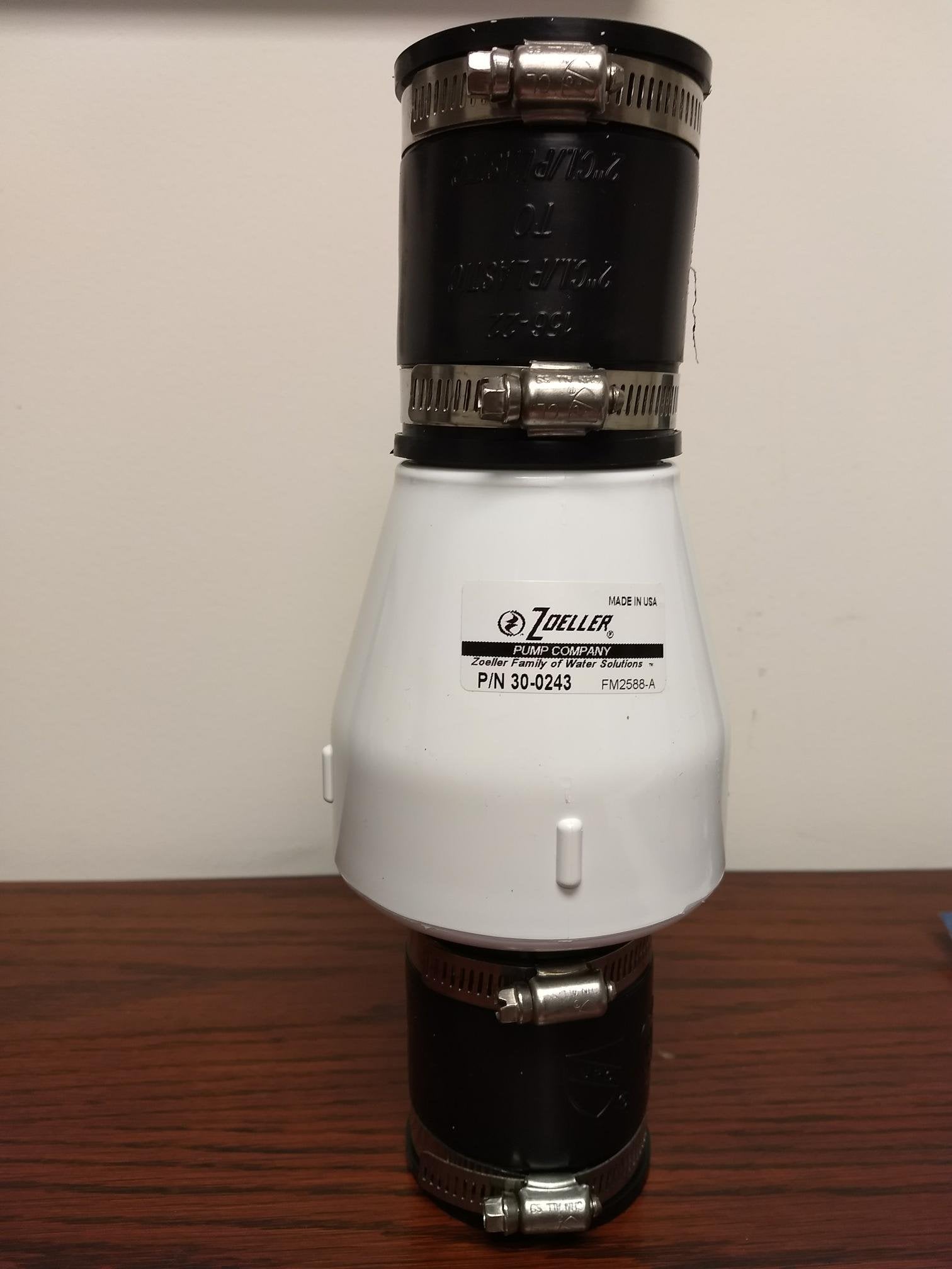 Two-inch PVC check valve with black end caps and metal hose clamps, white center section labeled Zoeller.