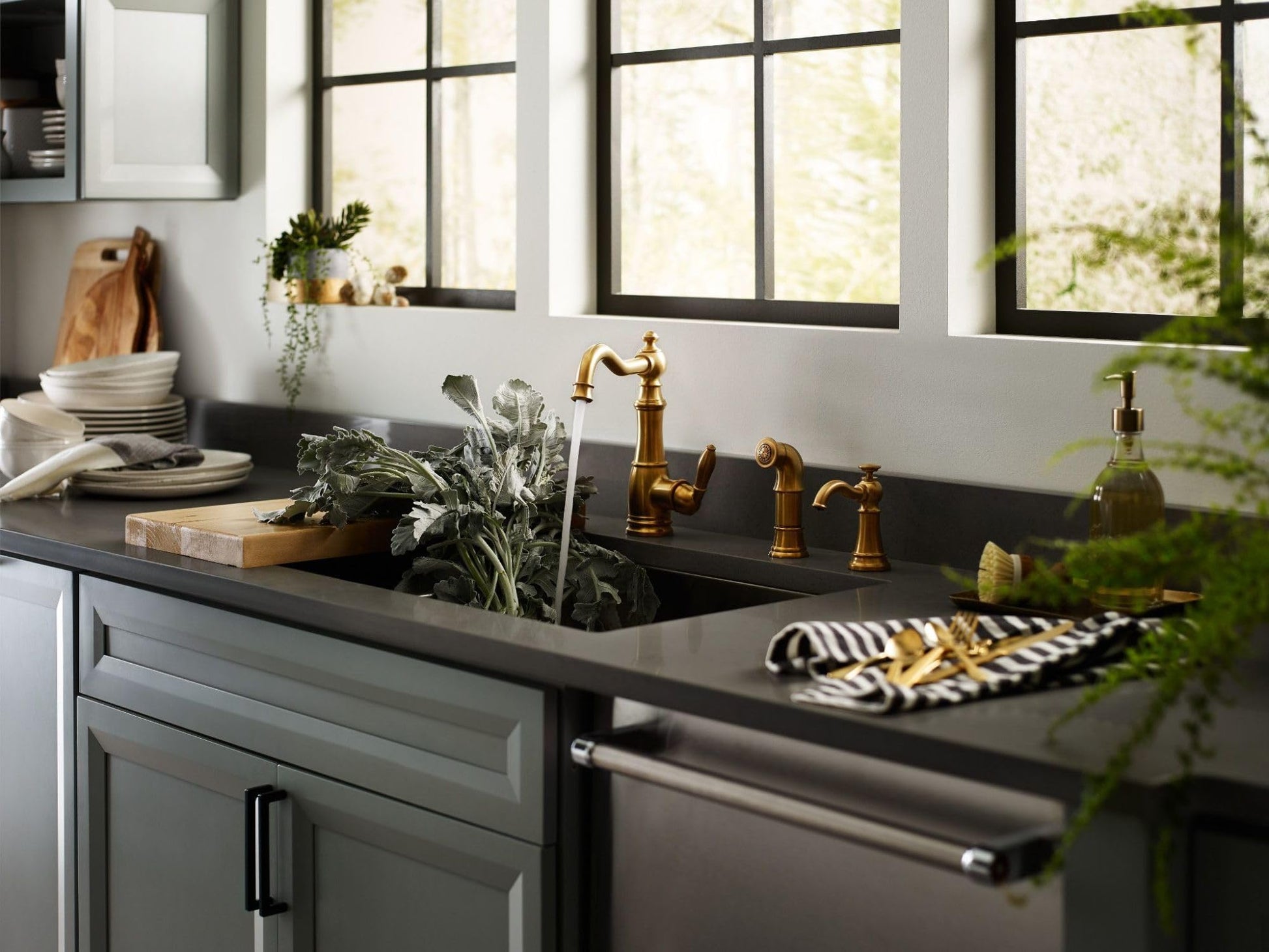 Brushed gold traditional soap dispenser mounted on kitchen countertop next to sink faucet and decorative bottle.