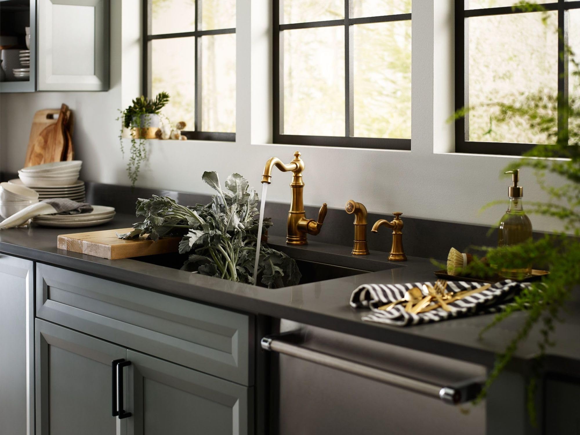 Brushed gold traditional soap dispenser mounted on kitchen countertop next to sink faucet and decorative bottle.