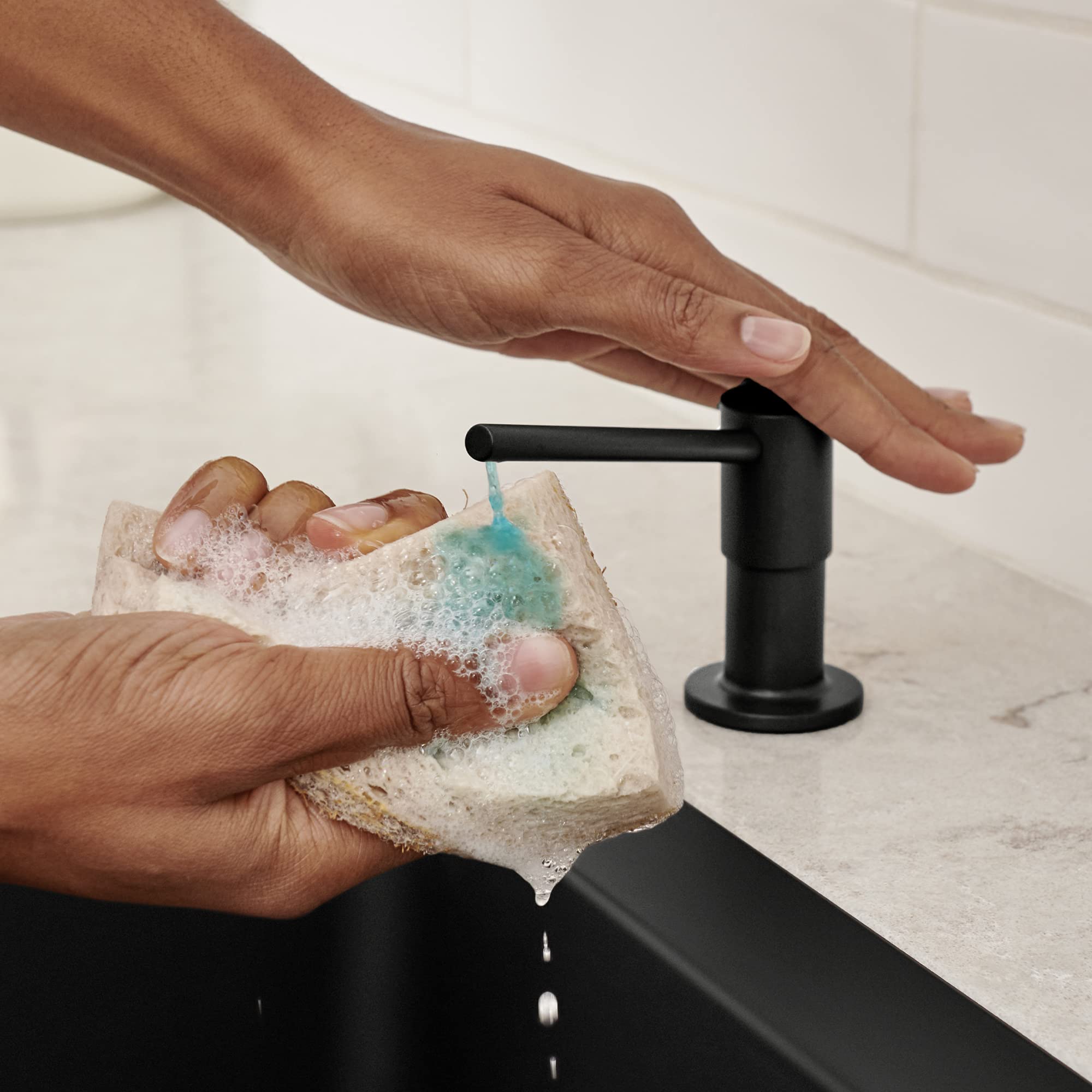 Coal black soap dispenser with cylindrical pump mounted on marble countertop with hands using soap.