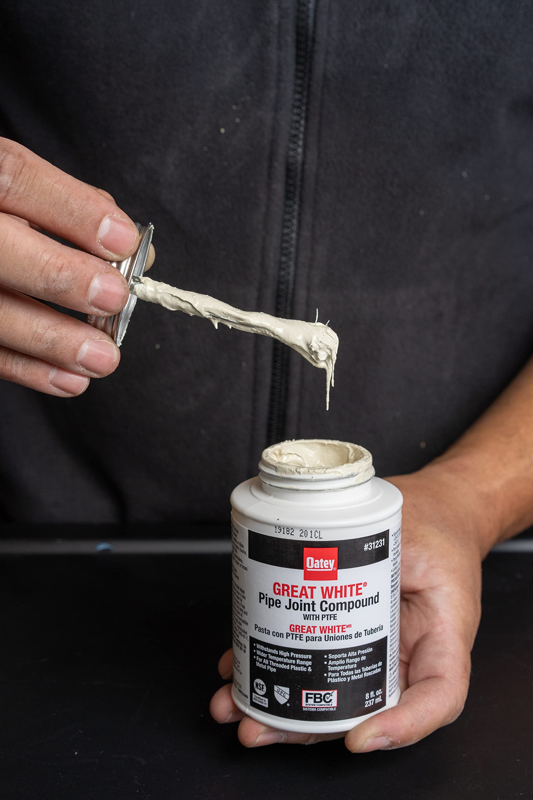 White Oatey Great White Pipe Joint Compound tube being held with applicator brush extending upward from open container.