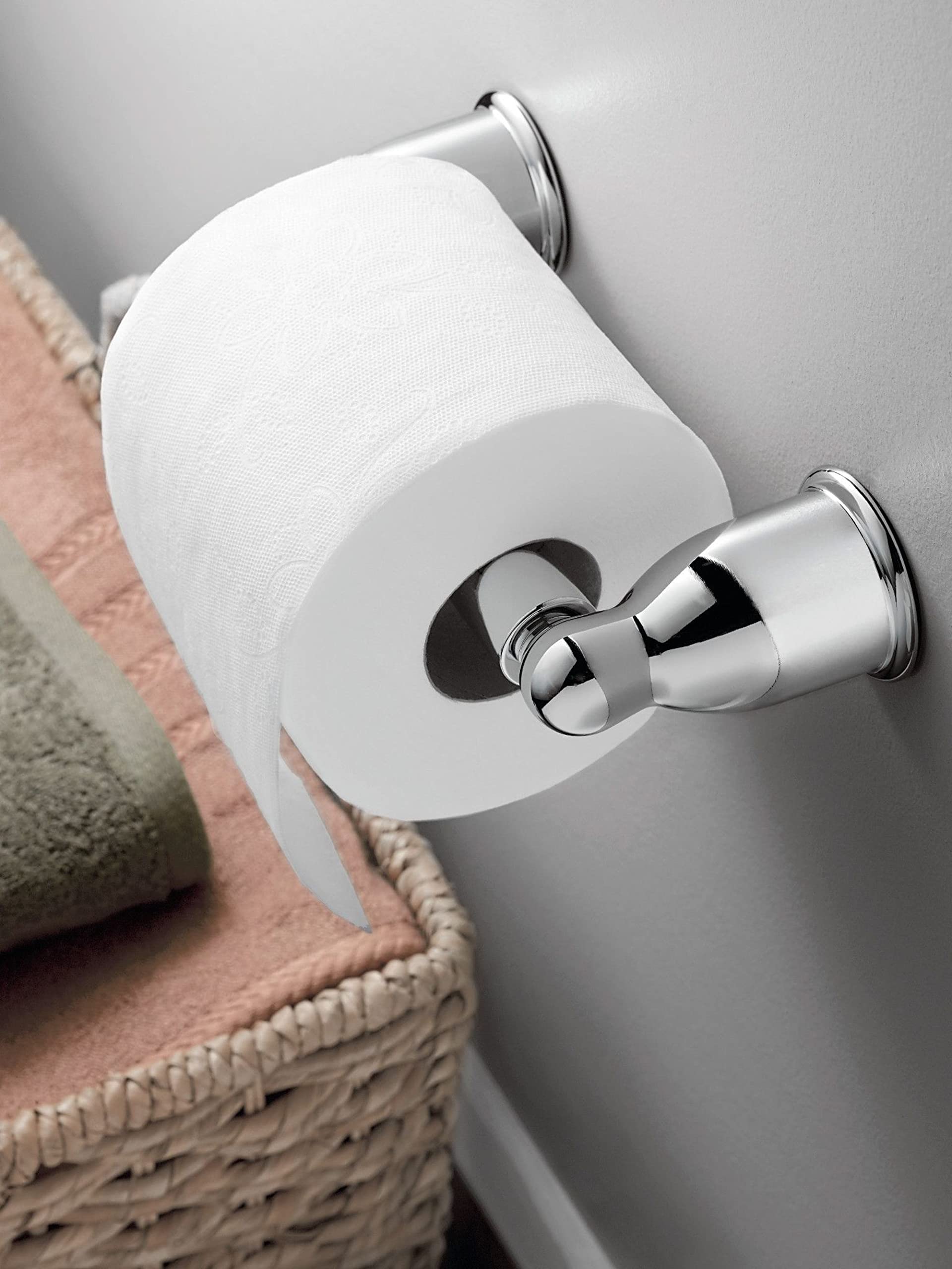 Chrome toilet paper holder mounted on white wall with white toilet paper roll loaded.