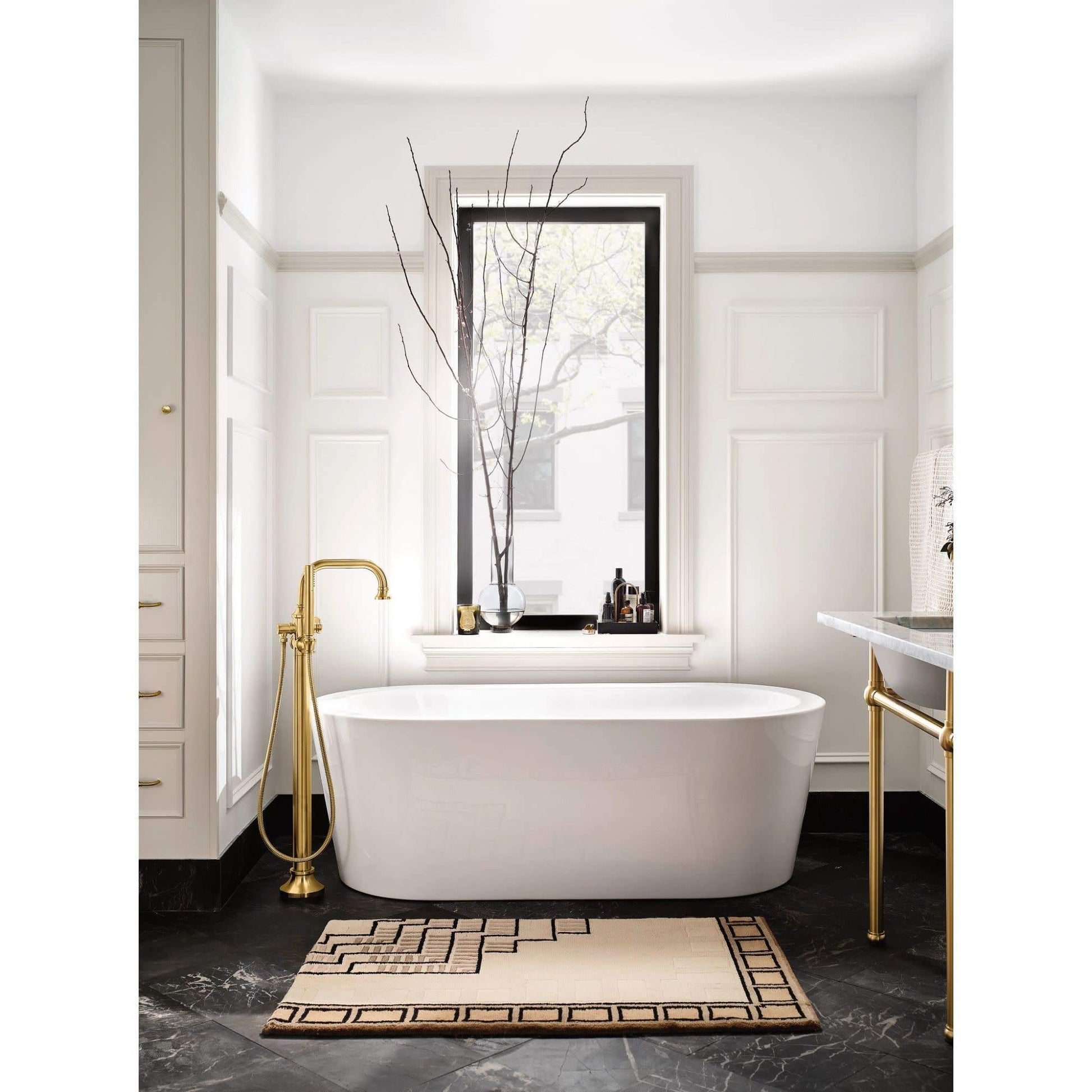 Matte black freestanding floor mount tub filler with single handle and attached handshower next to white soaking tub.