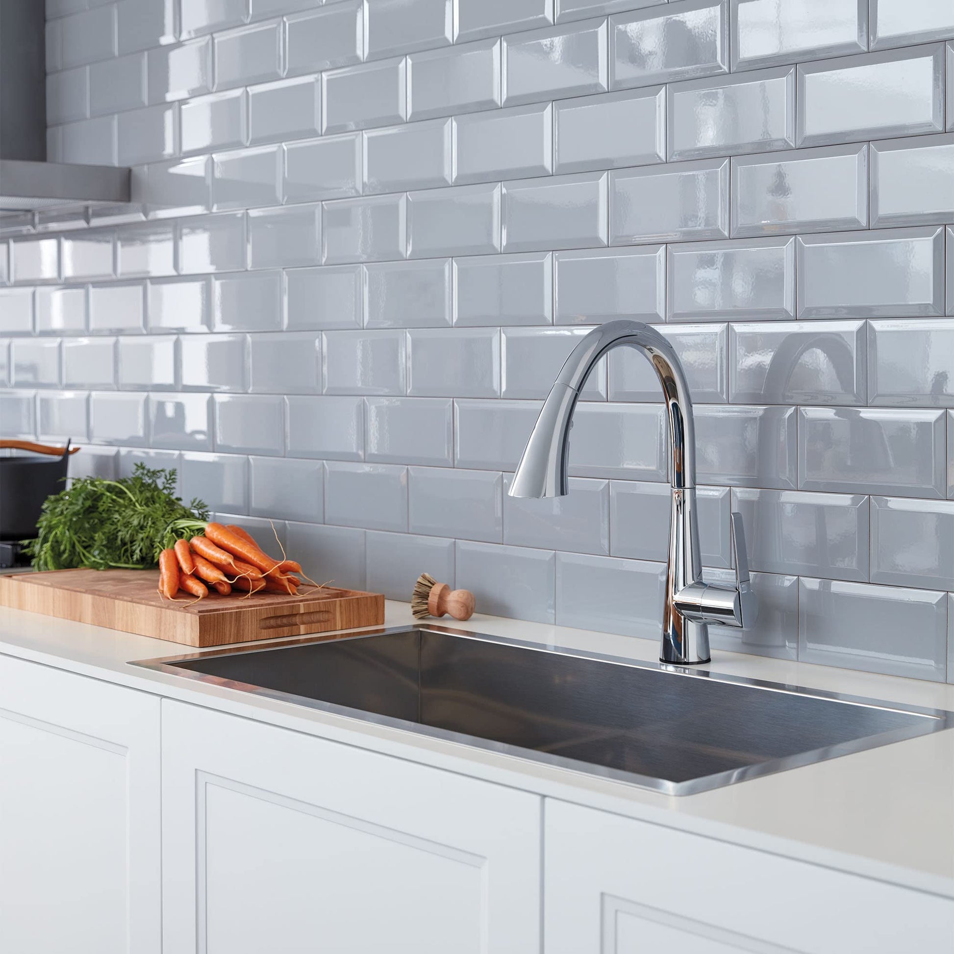Chrome pull-down kitchen faucet with curved spout mounted above stainless steel sink on white subway tile backsplash.