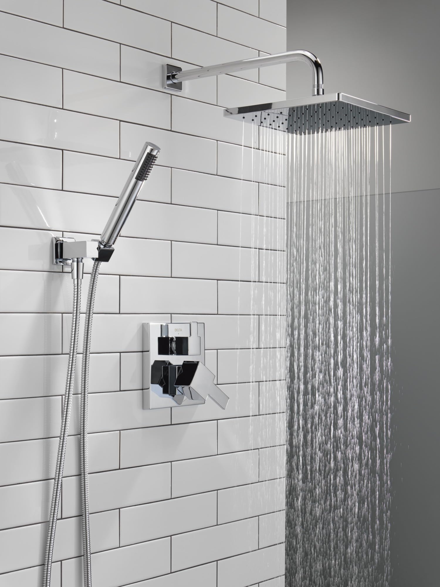 Chrome shower system with square raincan showerhead, curved arm, hand shower with hose, and wall-mounted valve control.