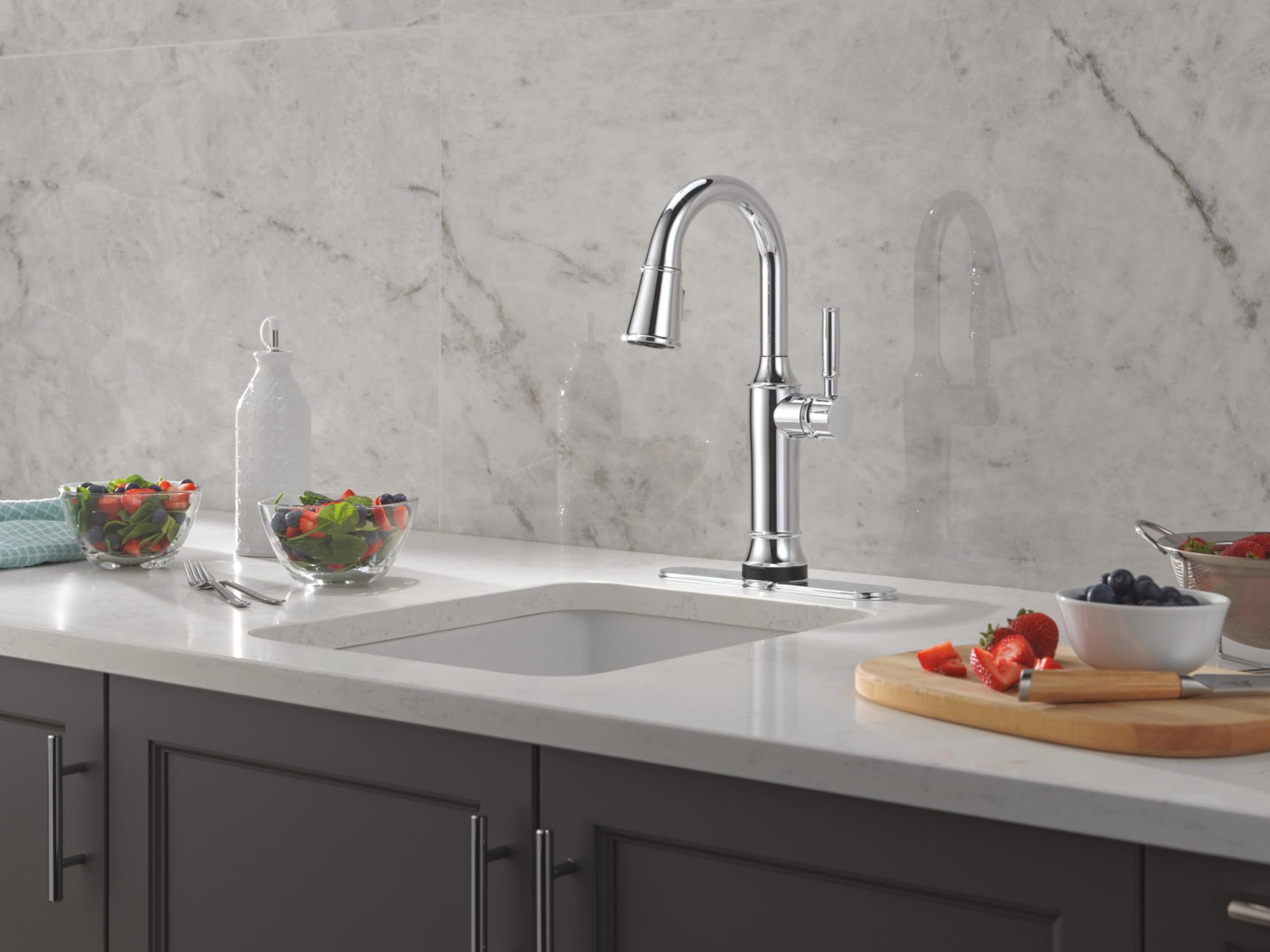 Chrome pulldown kitchen faucet with curved spout mounted on white countertop above sink.