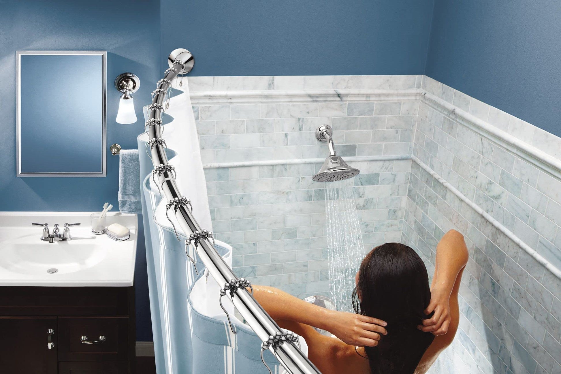 Chrome curved tension shower rod with rings holding clear shower curtain in bathroom with marble tile surround.