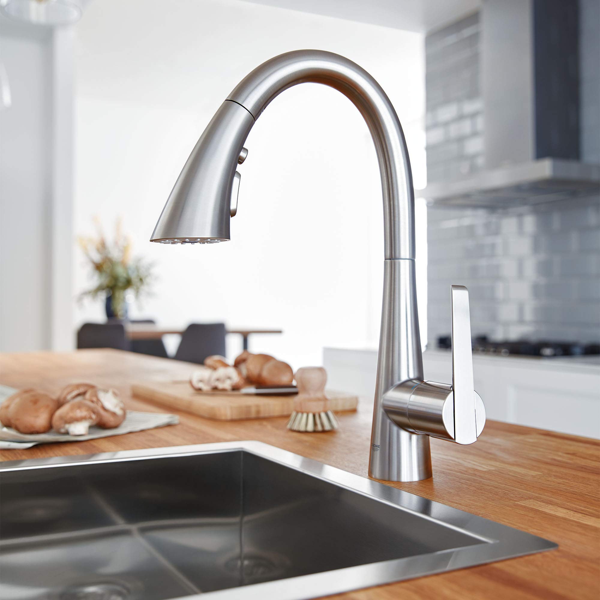 Stainless steel pull-down kitchen faucet with single lever handle and curved spout over sink.