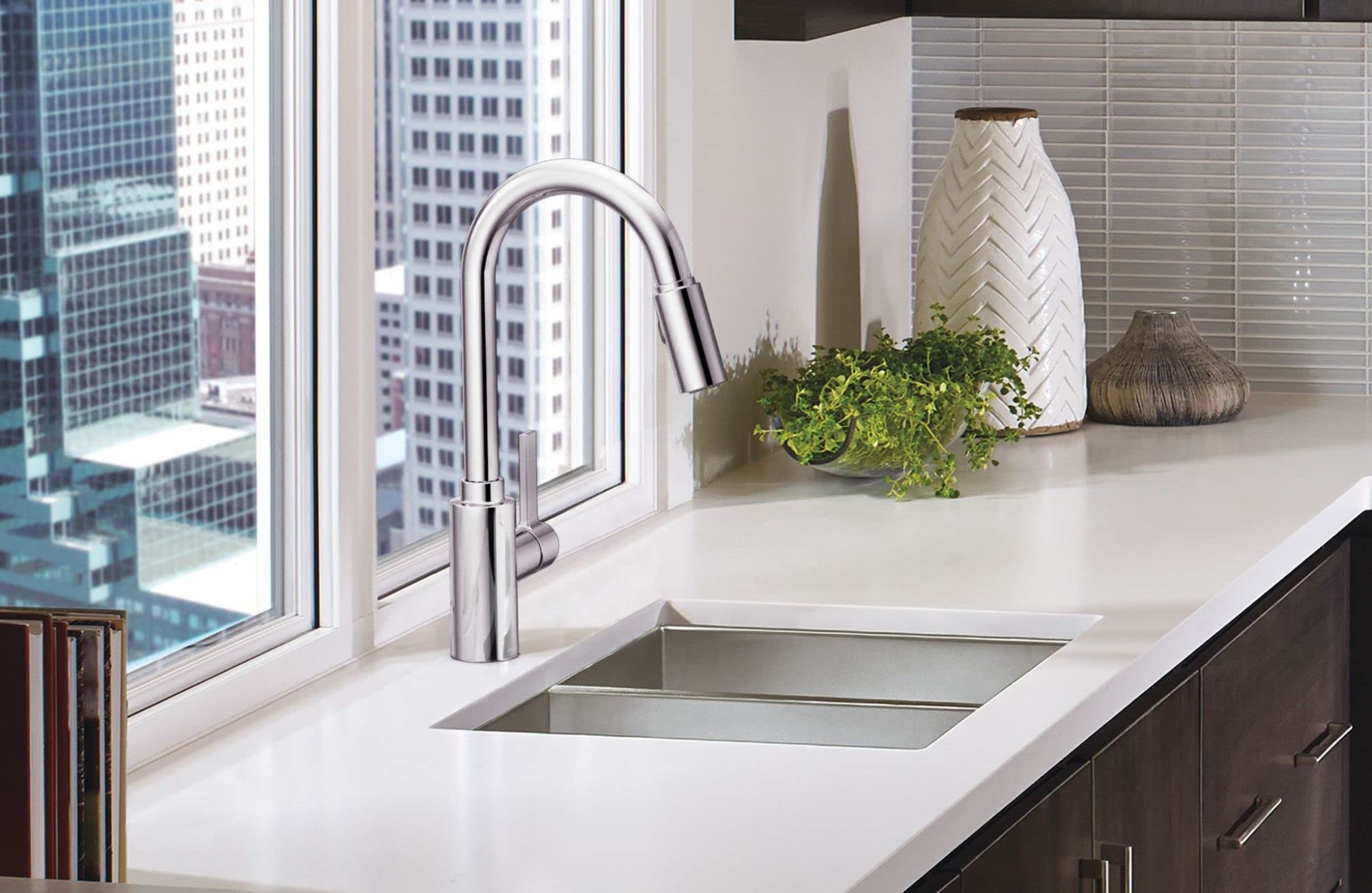 Chrome pull-down kitchen faucet with curved spout installed above rectangular sink in white countertop.
