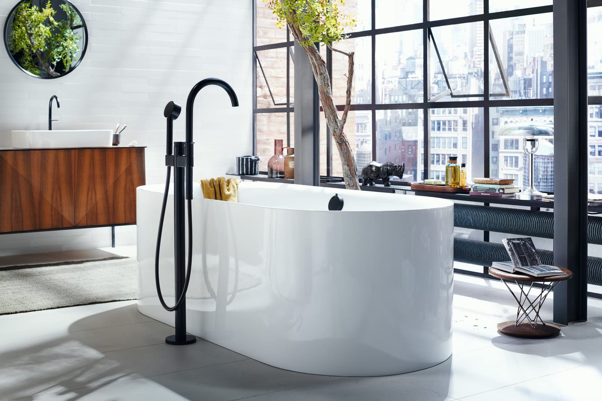 Matte black freestanding tub filler with curved spout and handheld showerhead installed on white freestanding soaking tub.