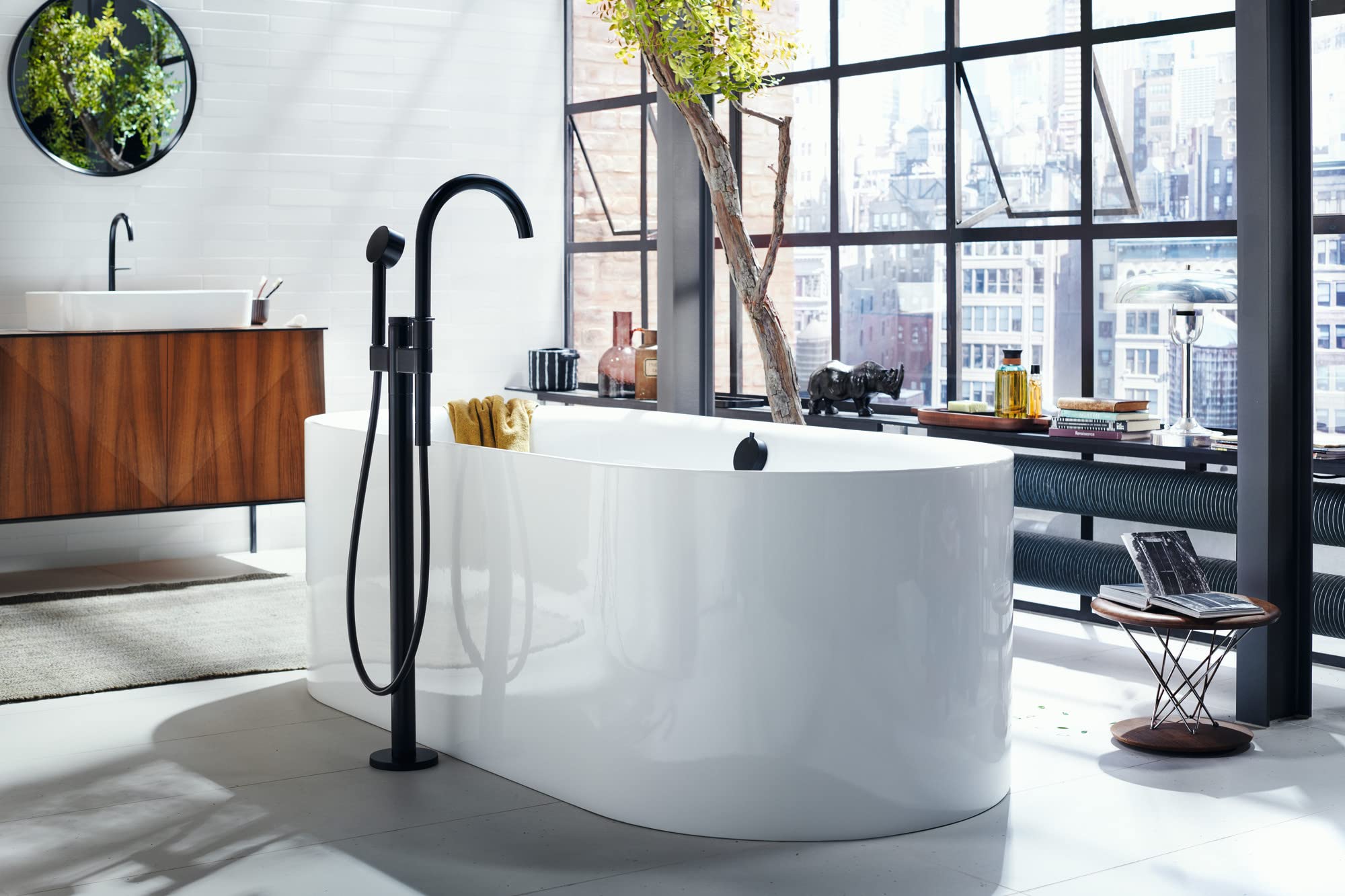 Matte black freestanding tub filler with curved spout and handheld showerhead installed on white freestanding soaking tub.