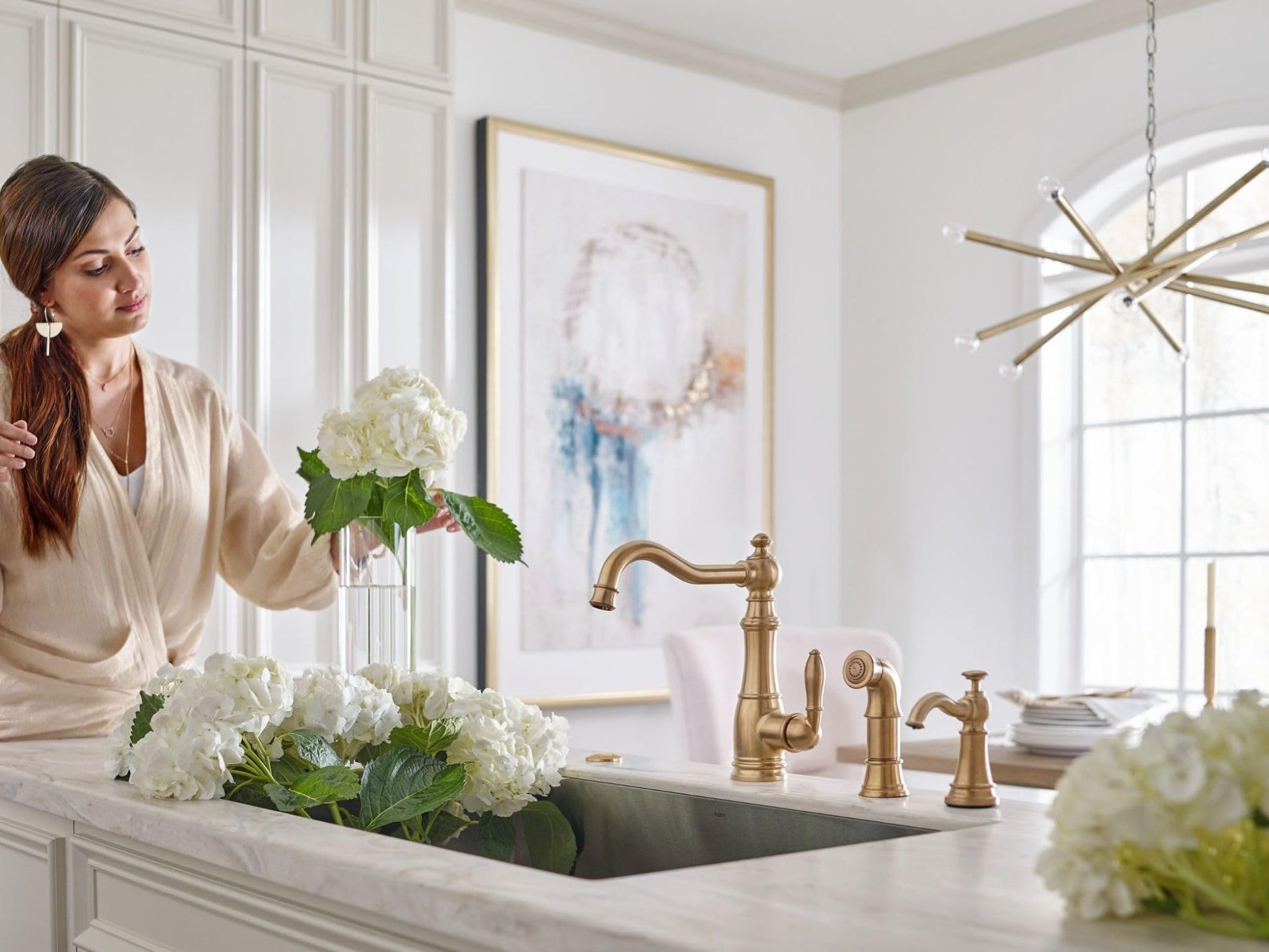Brushed gold traditional kitchen faucet with matching soap dispenser pump mounted on white countertop beside sink.