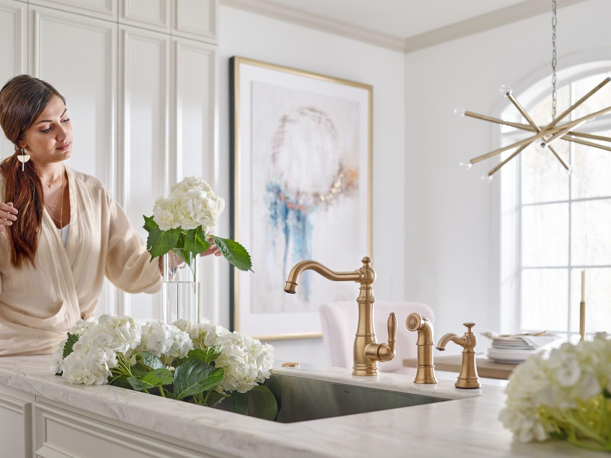 Brushed gold traditional kitchen faucet with matching soap dispenser pump mounted on white countertop beside sink.