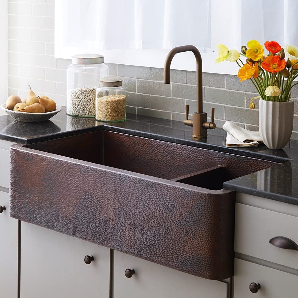 Antique copper farmhouse sink with two compartments and hammered finish surface texture installed in kitchen counter.