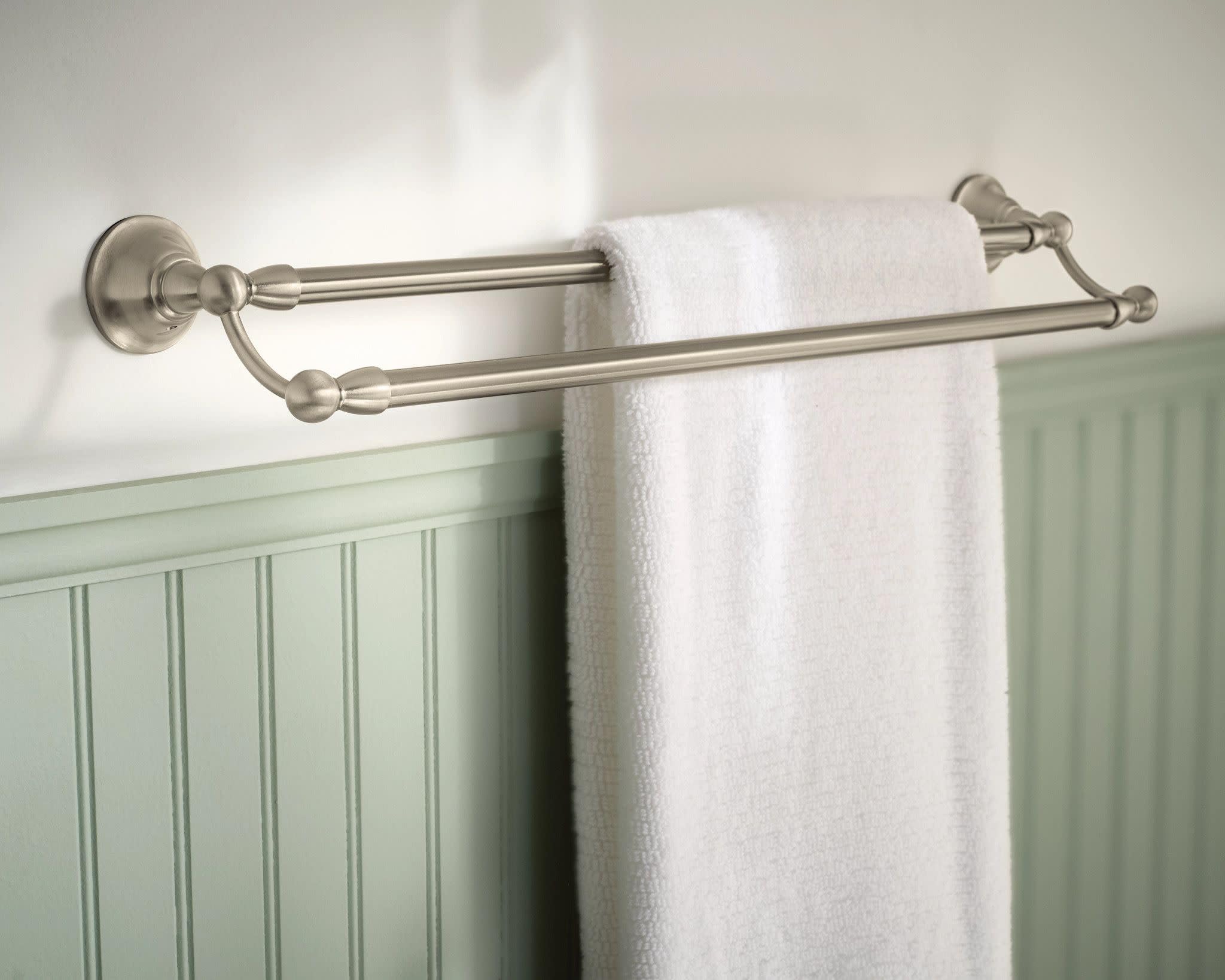Brushed nickel double towel bar mounted on white wall with white towel draped over both bars.