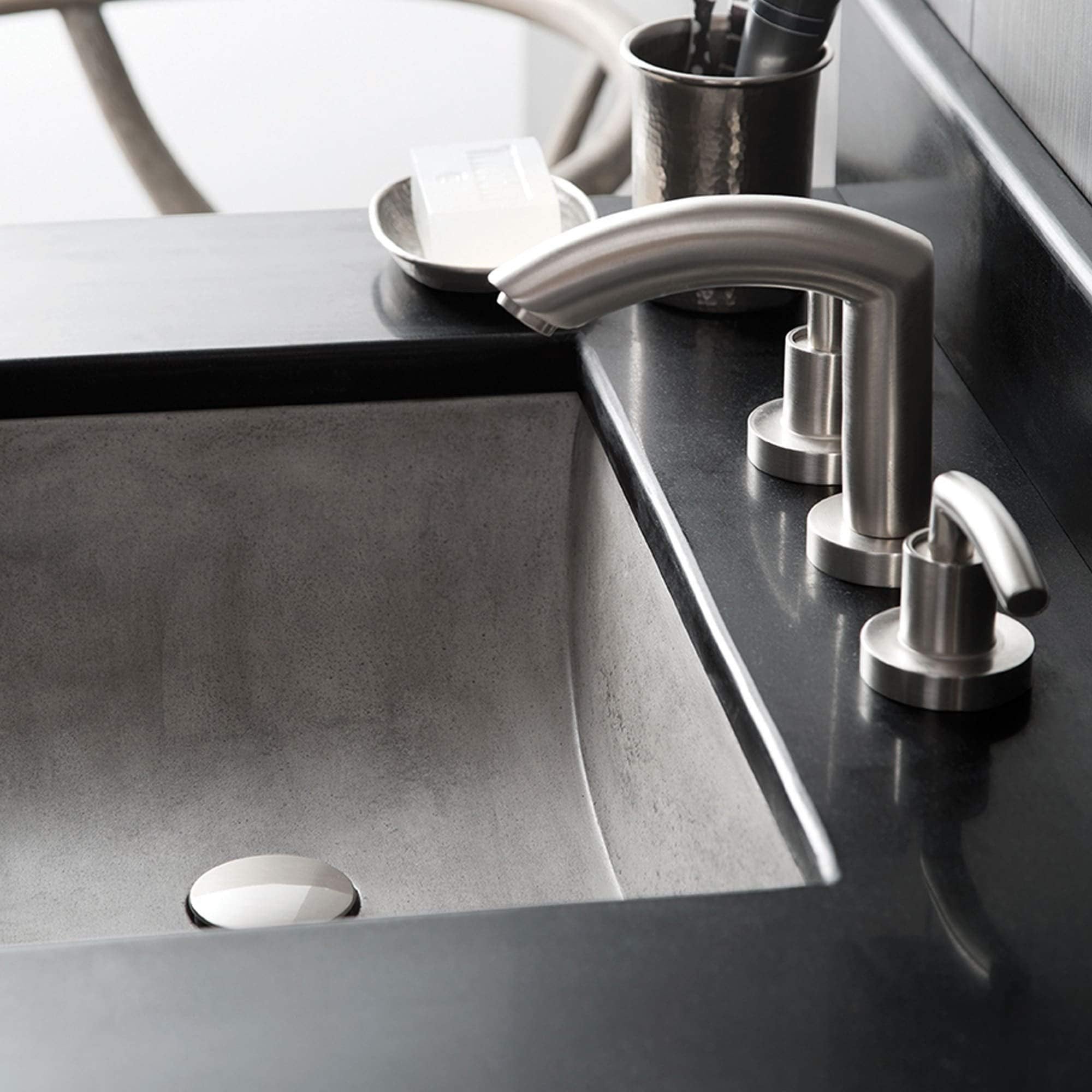 Pearl-colored undermount bathroom sink with curved edges and stainless steel faucet on dark countertop.