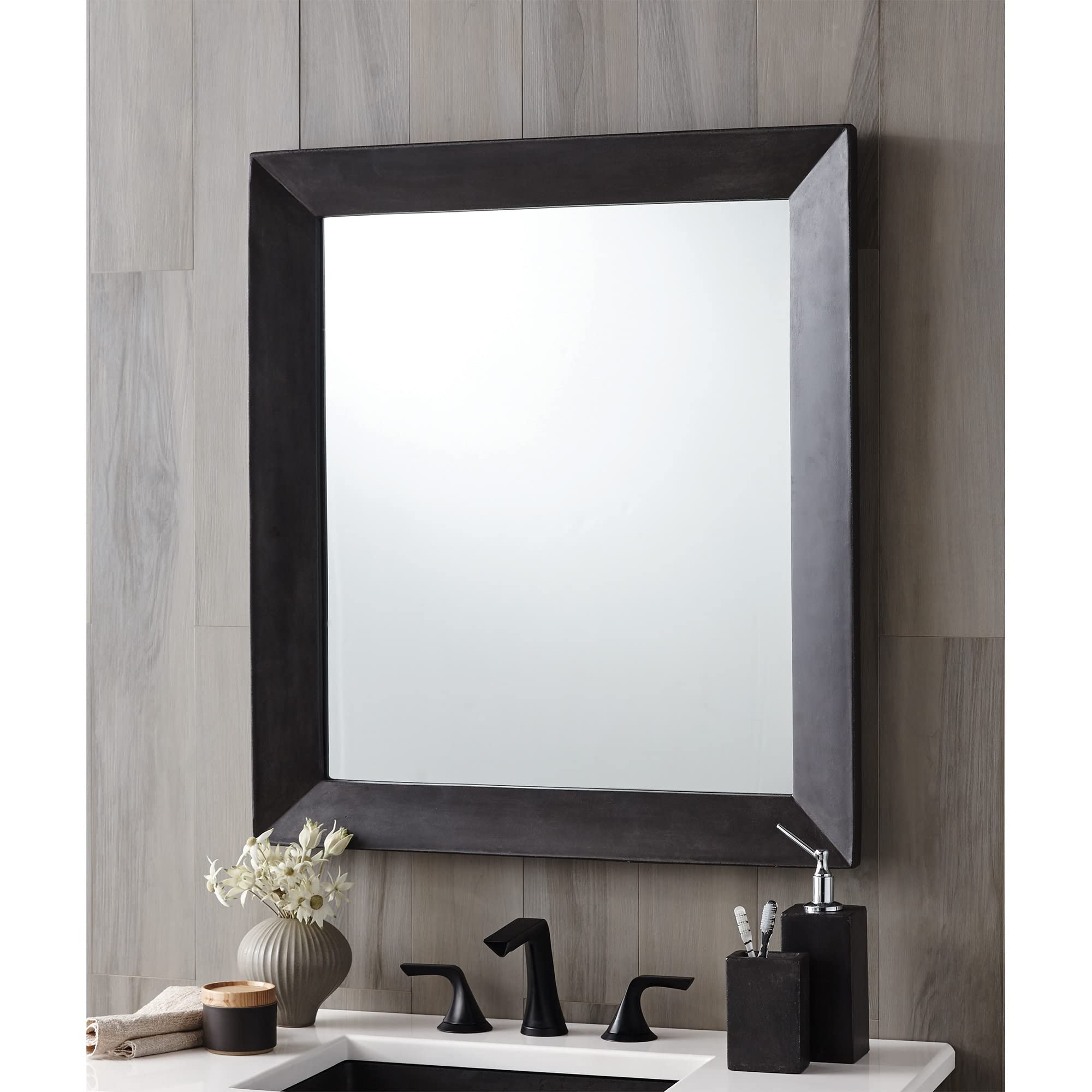 Square mirror with black frame and pearl accent trim mounted above bathroom sink with black faucet and accessories.