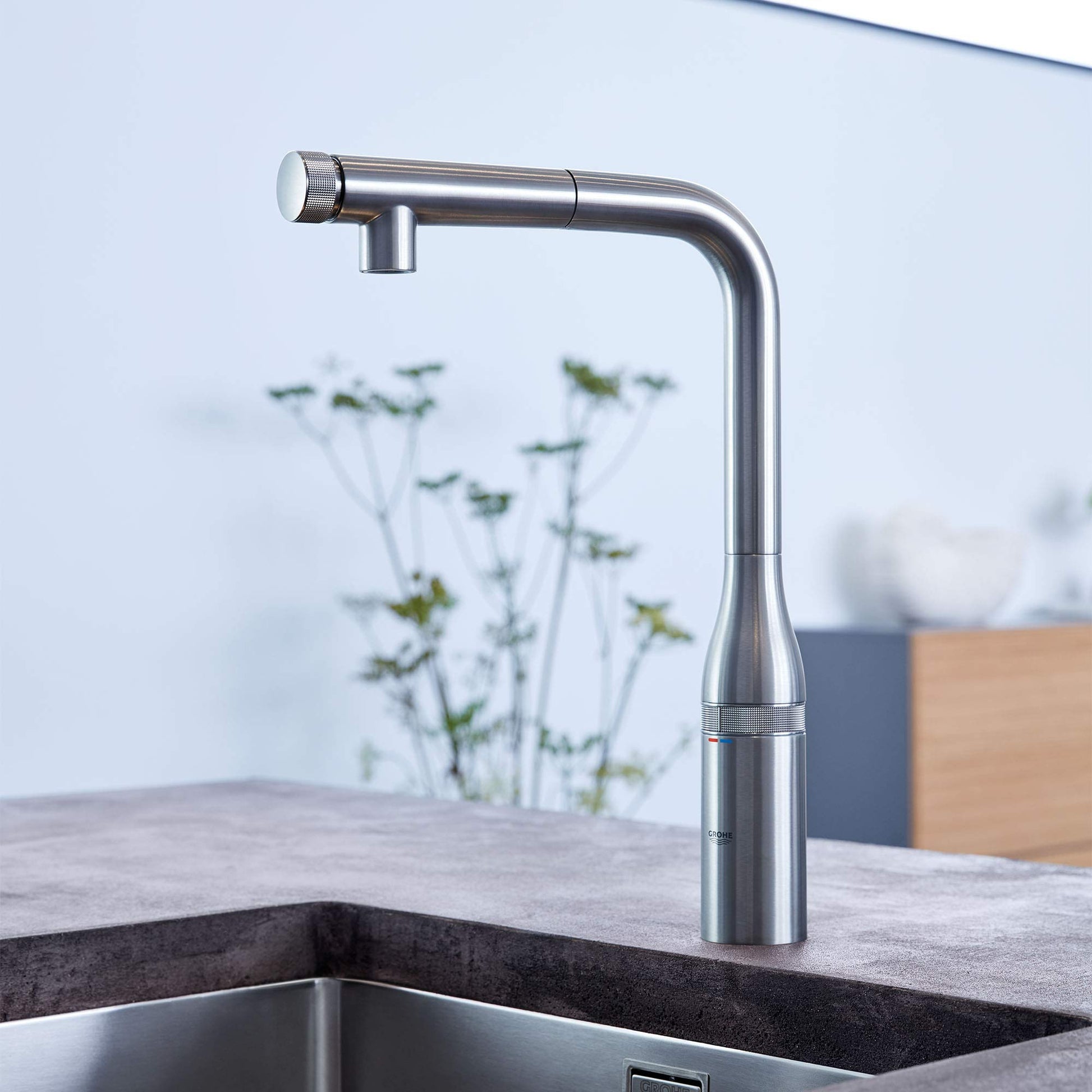 Grohe Essence stainless steel pull-out kitchen faucet with single spray nozzle and angled spout over sink.