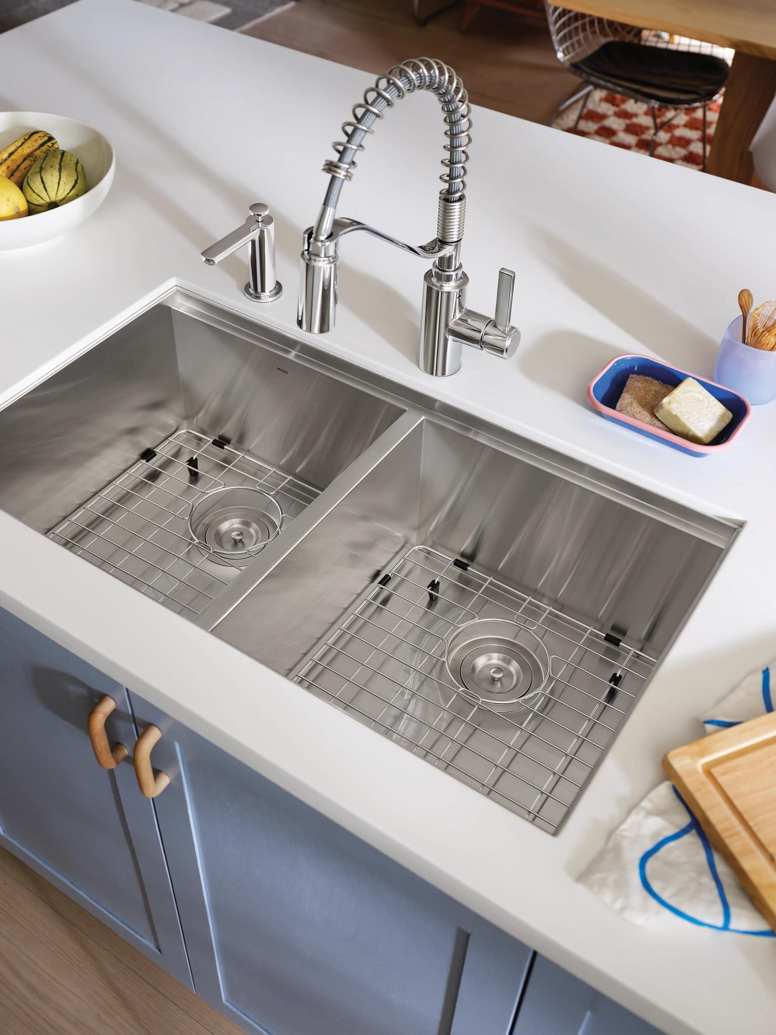 Stainless steel double bowl undermount kitchen sink with two drain grids, spiral faucet, soap dispenser, and surrounding coun