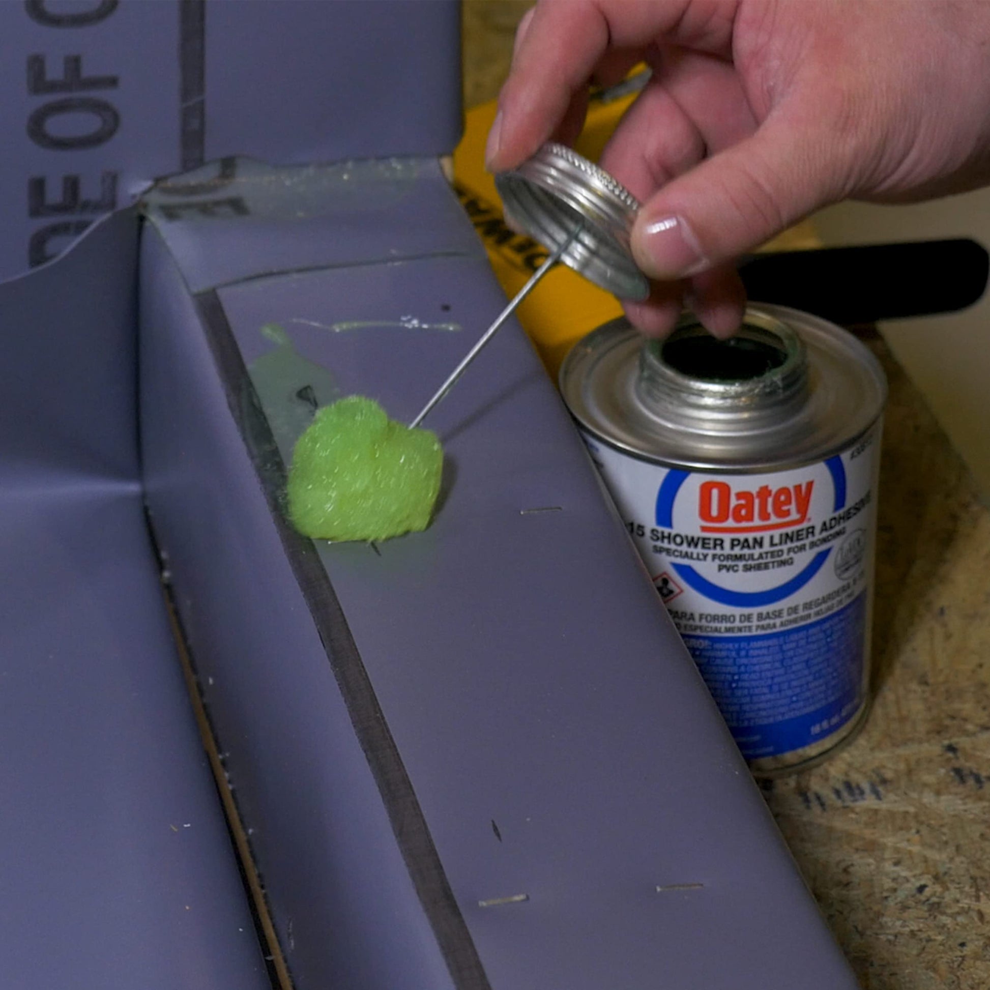 Hand holding Oatey solvent cement can with brush applicator, applying white adhesive to PVC pipe.