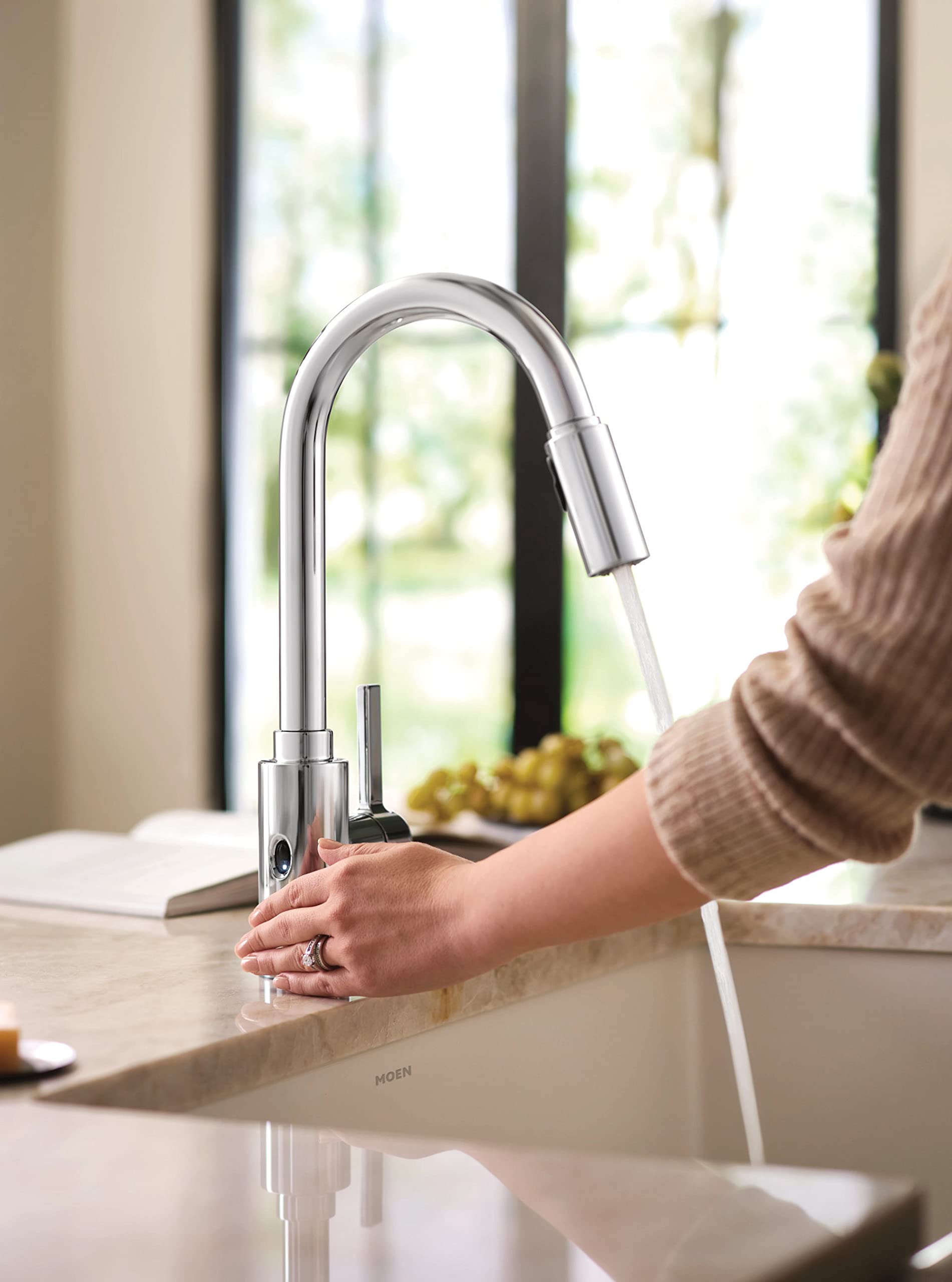 Chrome kitchen faucet with high arc pulldown spout and single handle, hand positioned near sensor activation area.