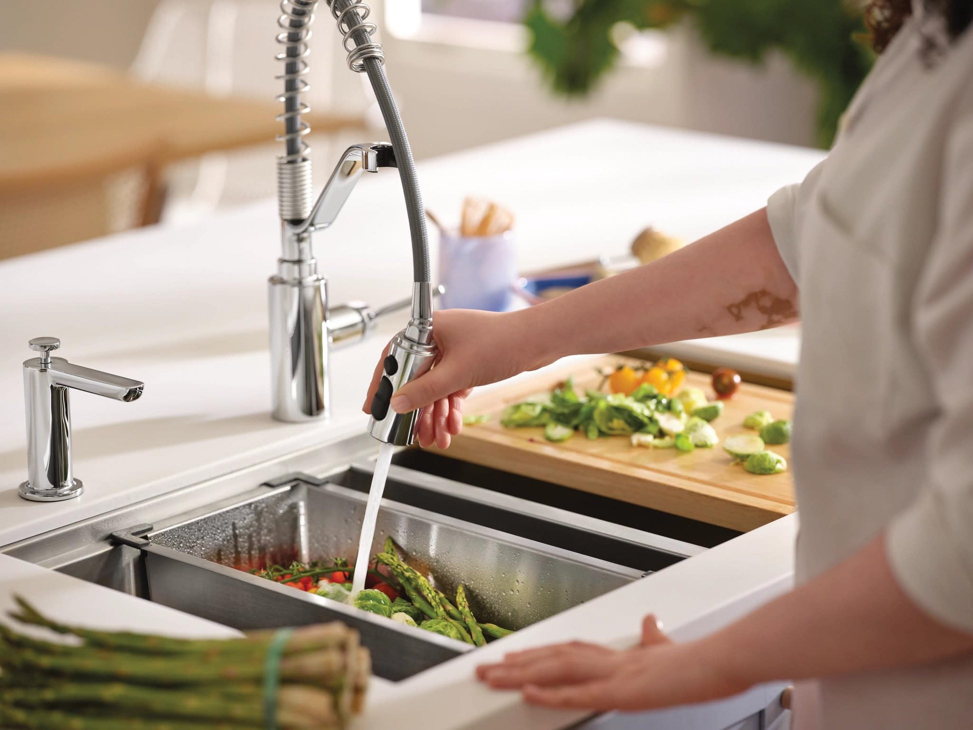 Stainless steel double bowl undermount kitchen sink with pull-down faucet, drying rack, and cutting board in use with vegetab