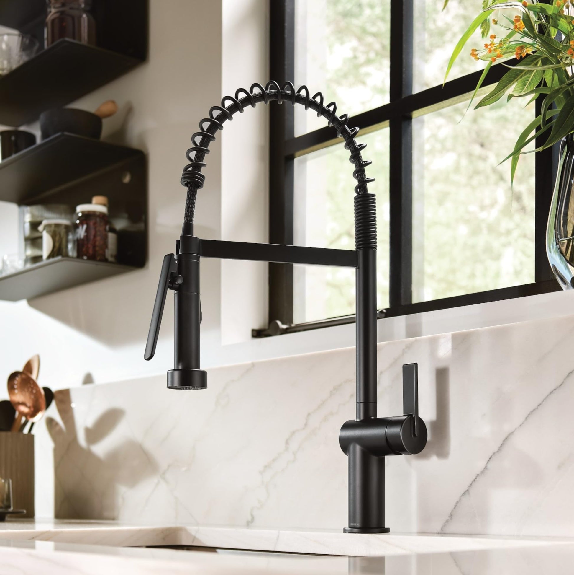 Matte black pre-rinse spring kitchen faucet with coiled hose and single handle mounted on white marble countertop.