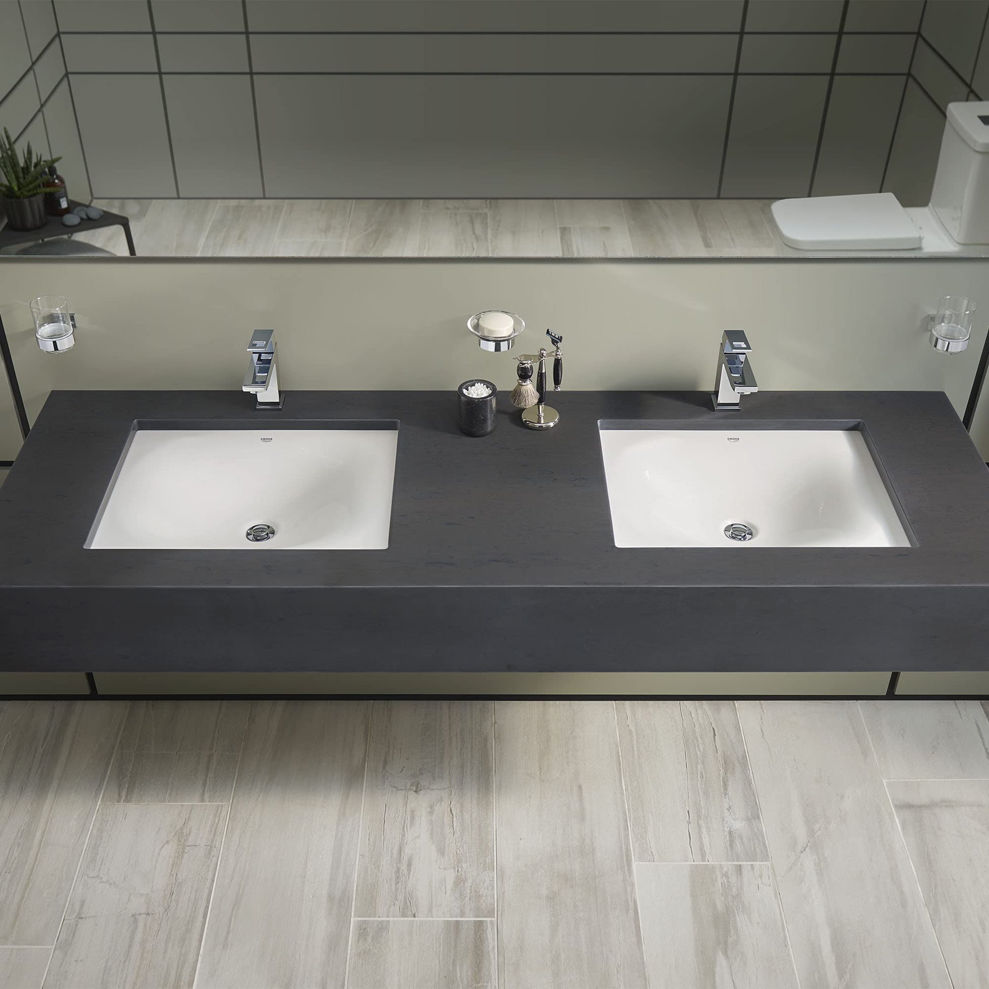 White rectangular undermount sink with chrome drain and faucet holes in dark vanity countertop.