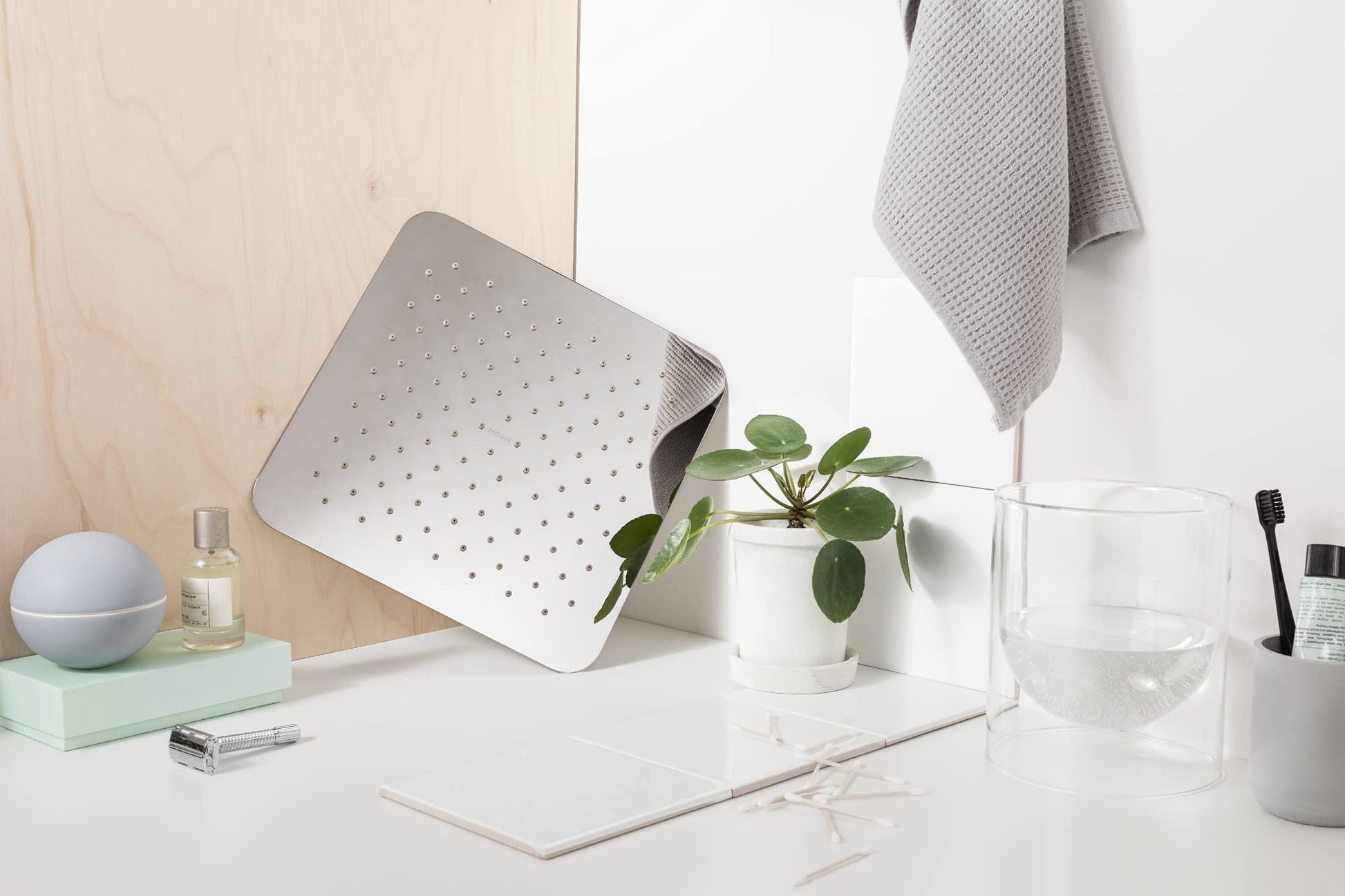 Chrome square rainshower head with perforated face and angled mounting bracket on white surface.