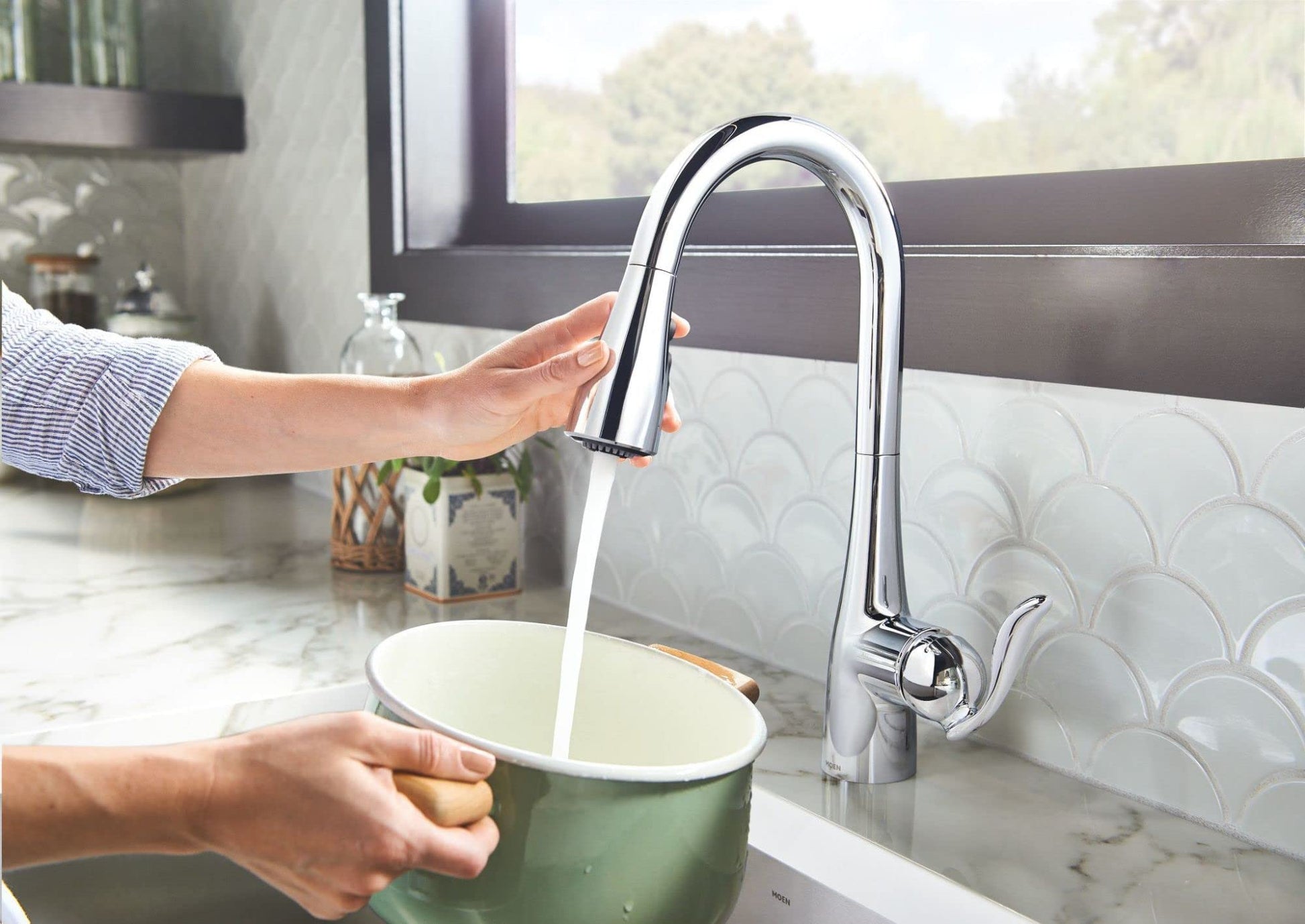 Chrome kitchen faucet with curved spout and pull-down sprayer over marble countertop sink.