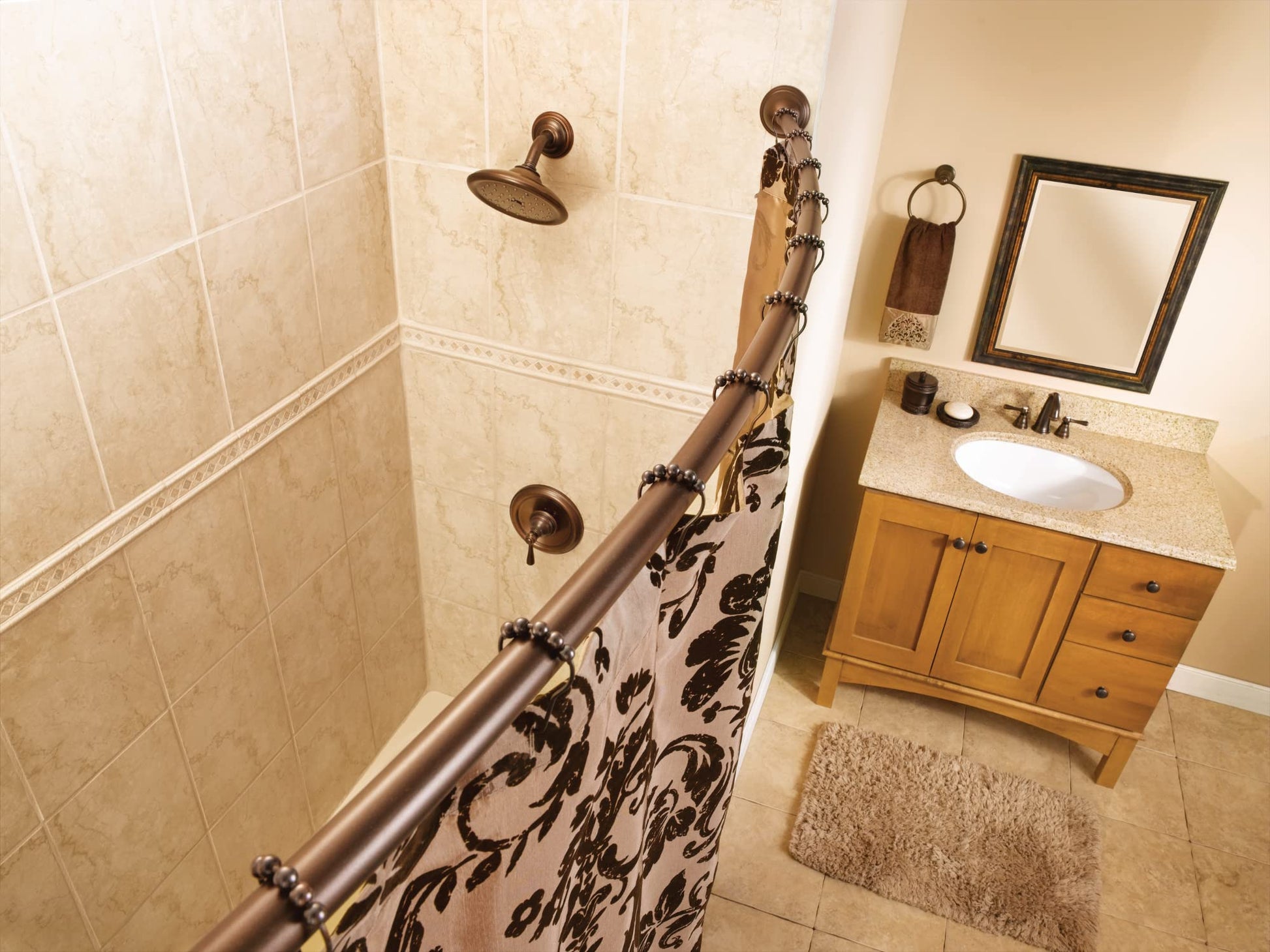 Oil rubbed bronze showerhead mounted on shower wall in beige tiled bathroom with matching fixtures.