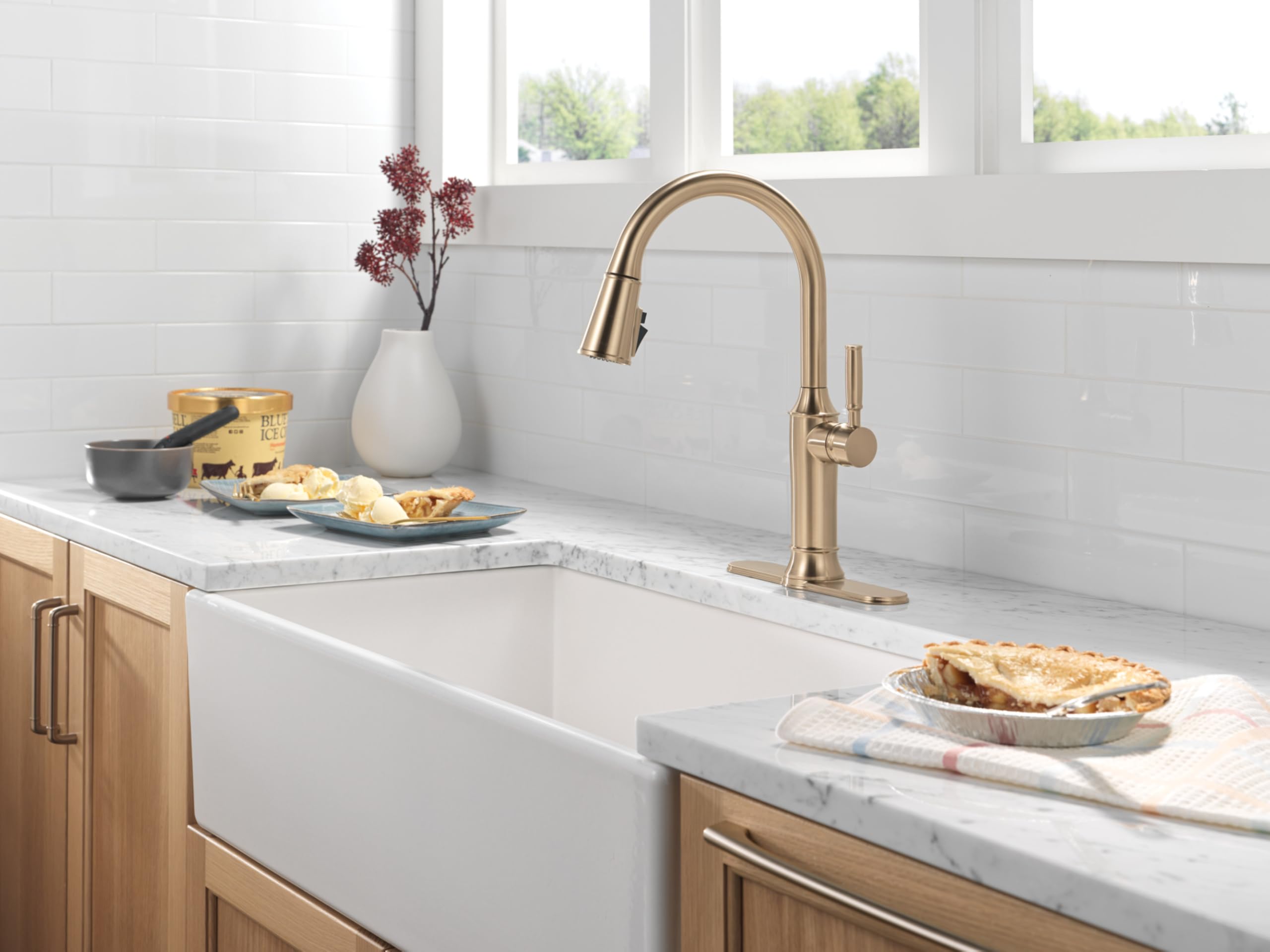 Champagne bronze pulldown kitchen faucet with curved spout and single handle above white farmhouse sink.