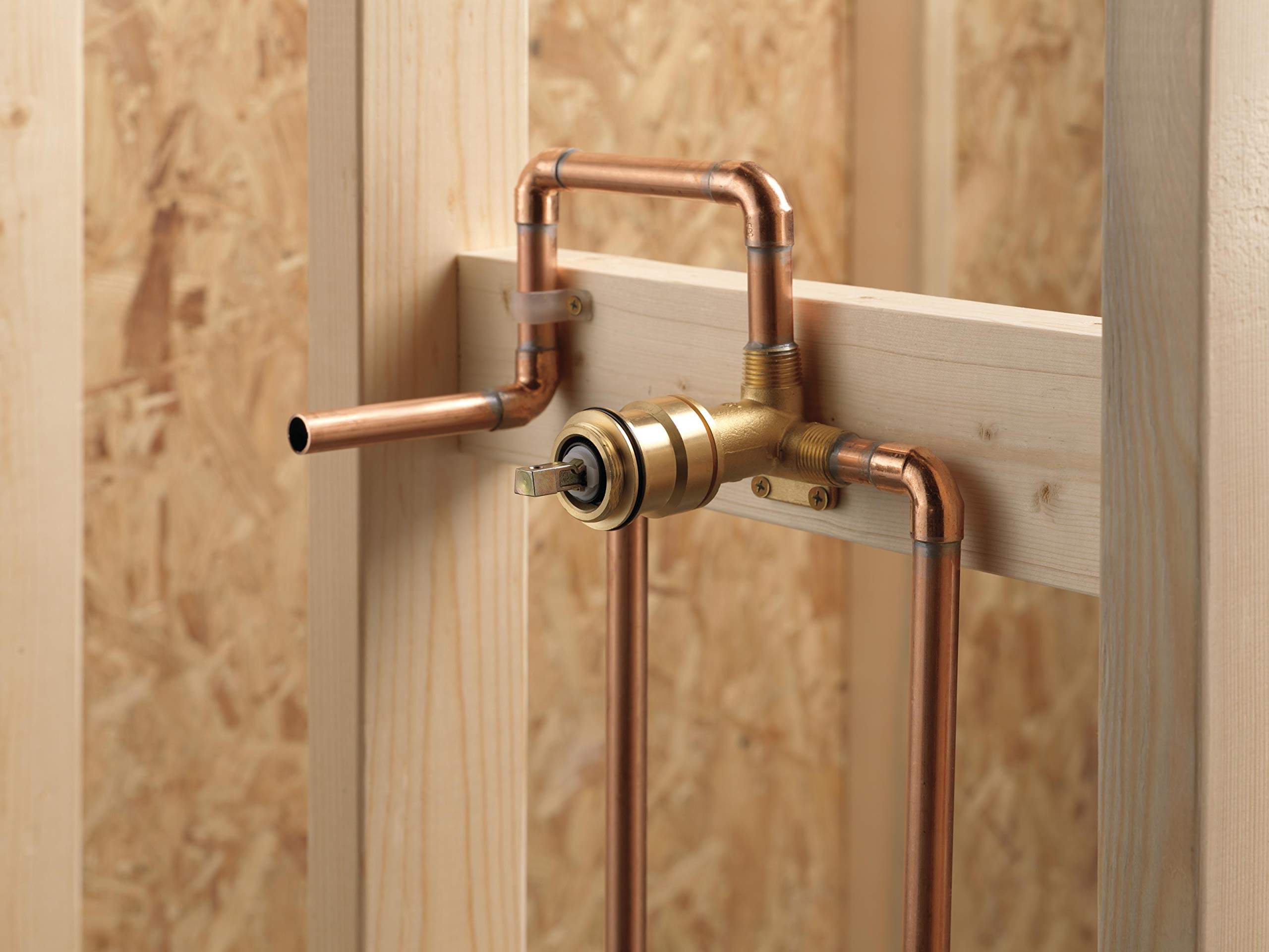 Copper wall-mount faucet rough-in with single handle lever and exposed plumbing pipes against wooden backing.
