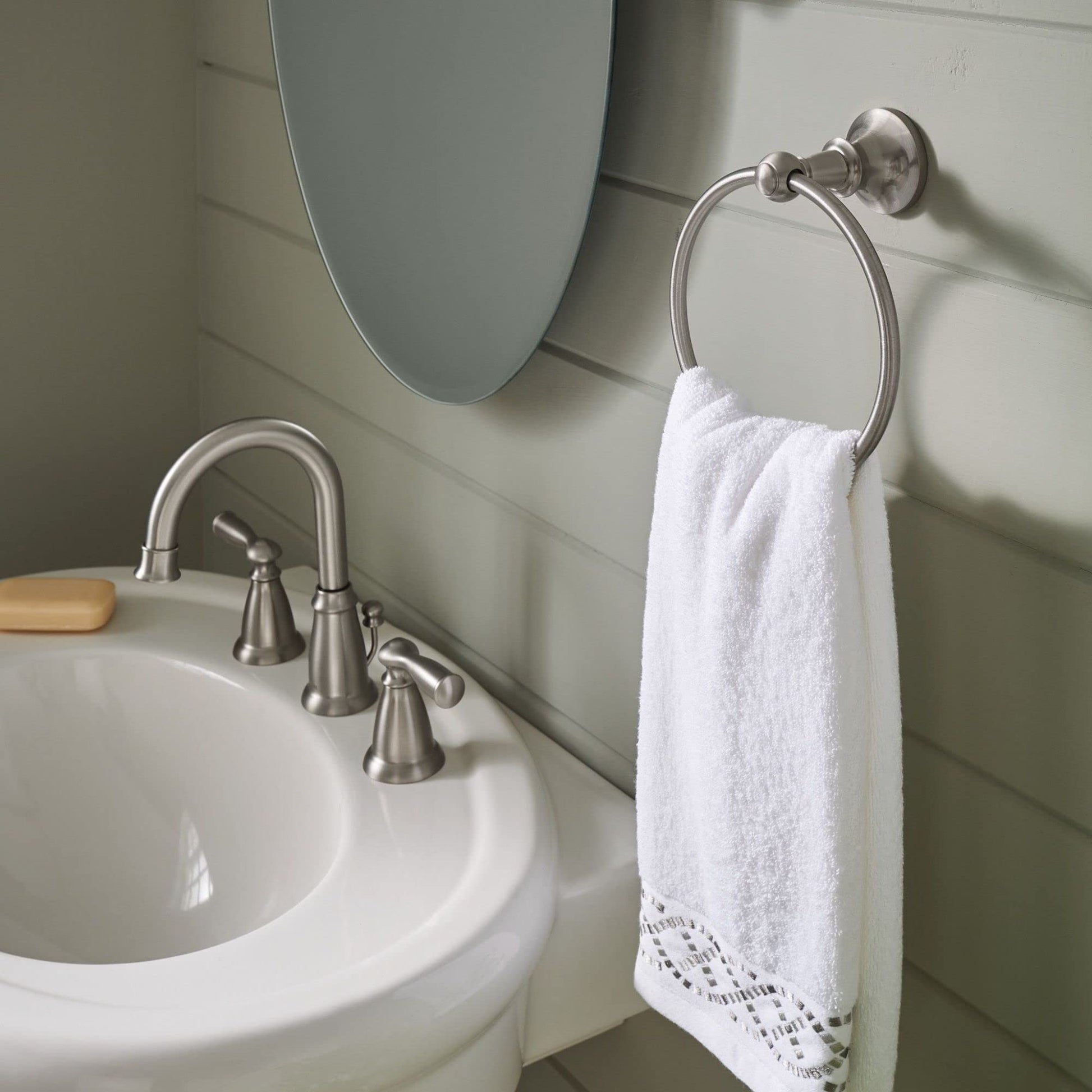 Brushed nickel wall-mounted towel ring with white towel hanging from circular chrome bar mounted on bathroom wall.