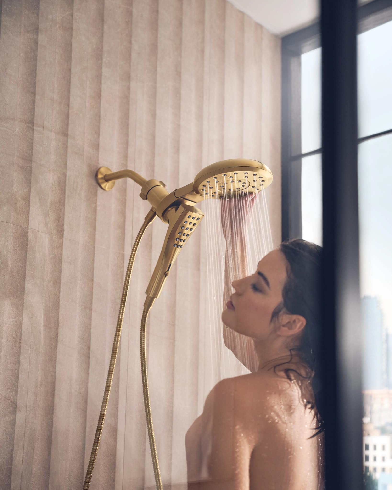 Brushed gold shower system with dual showerheads and handheld wand mounted on bathroom wall.