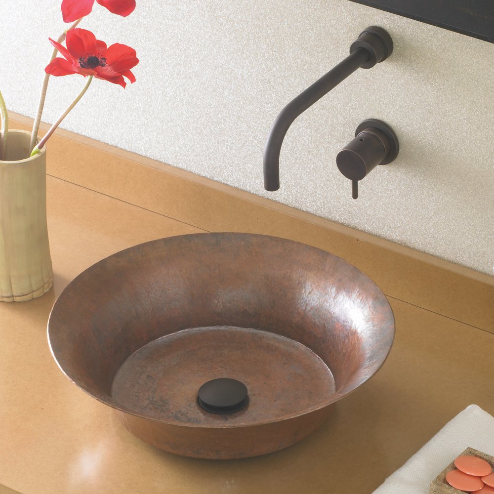Hammered copper vessel sink with curved walls and black wall-mounted faucet on light countertop.