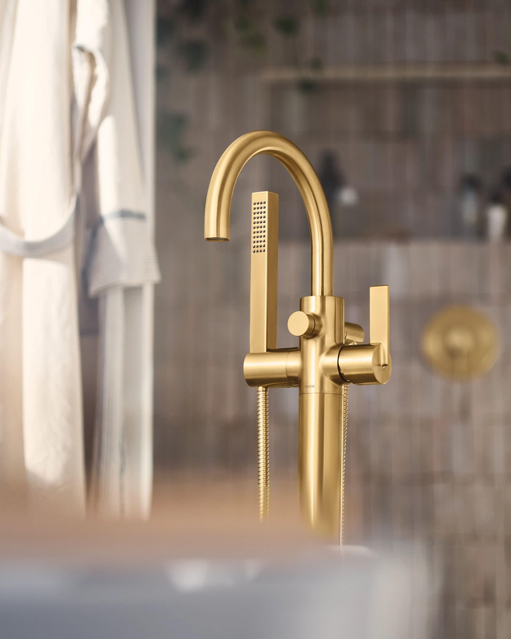 Brushed gold freestanding tub filler with curved spout, single lever handle, and detachable handshower on hose.