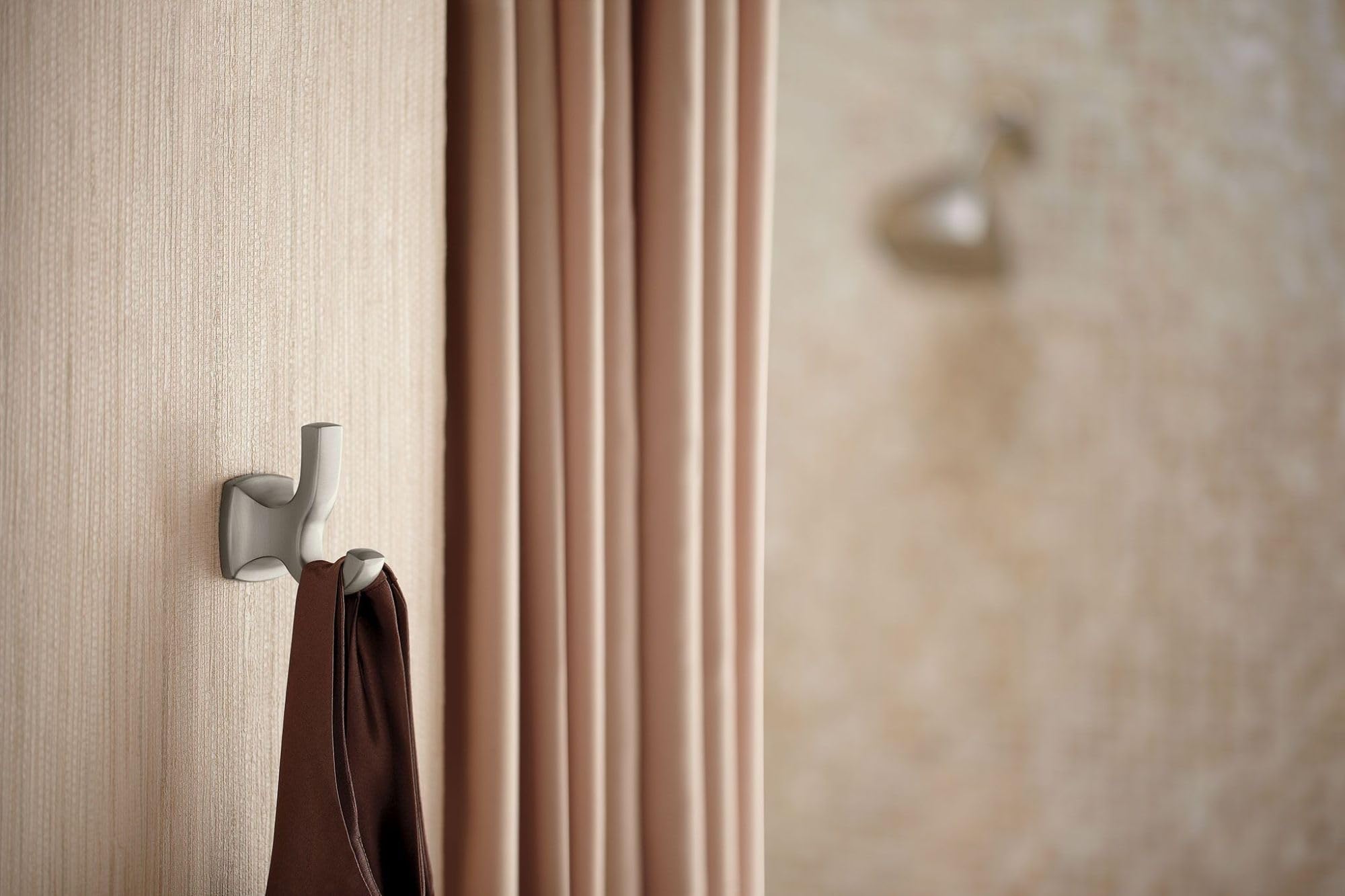 Brushed nickel double robe hook mounted on beige textured wall with towel hanging from one hook.
