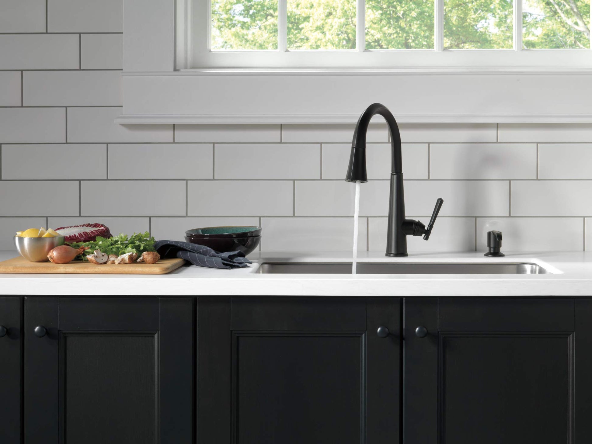 Matte black metal soap dispenser pump standing on kitchen counter next to sink faucet.