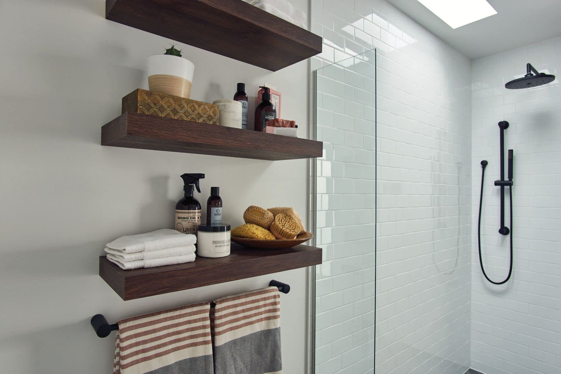 Black towel bar mounted below wooden shelf in modern bathroom with striped towel hanging.