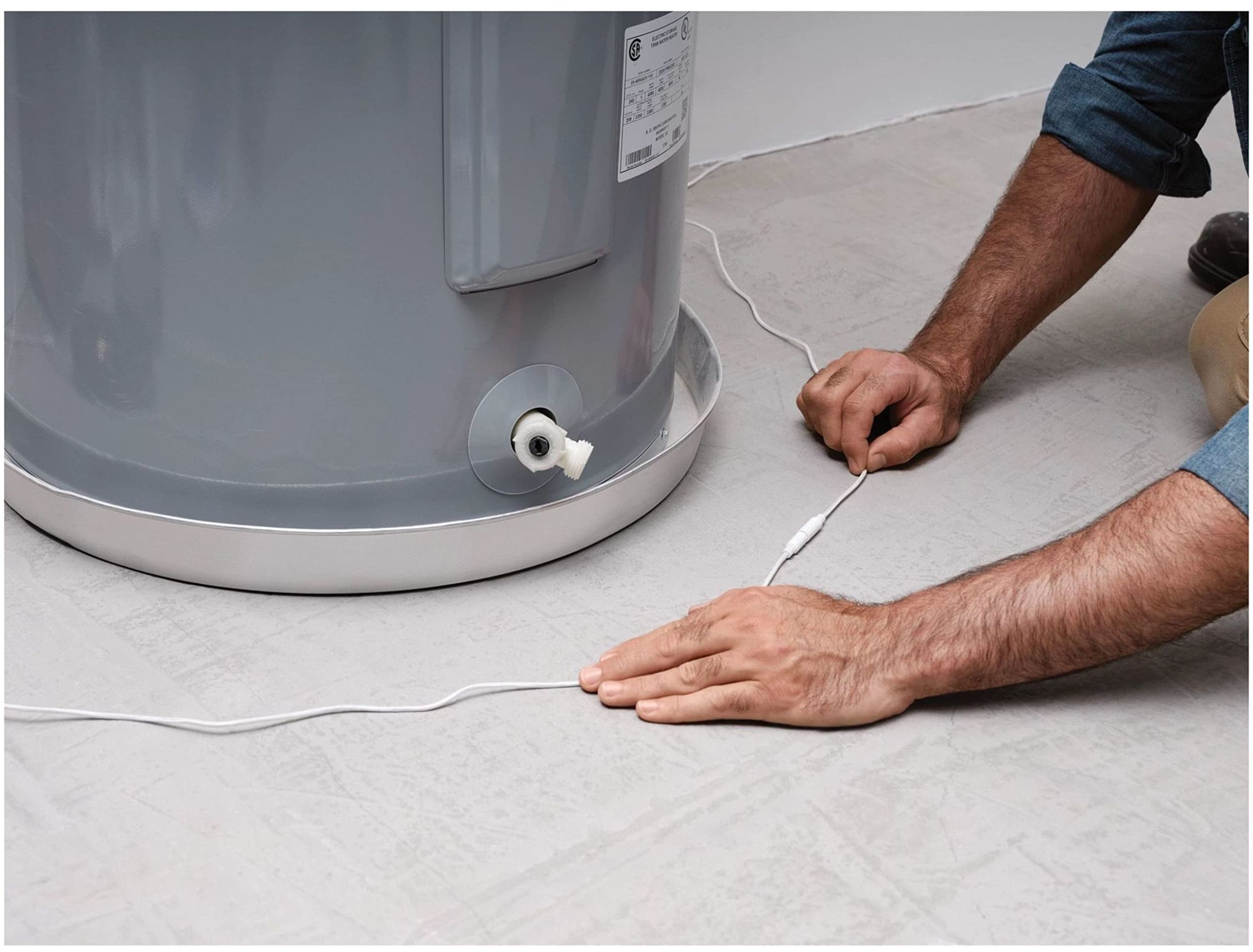 White sensing cable being positioned on floor next to water heater by two hands.