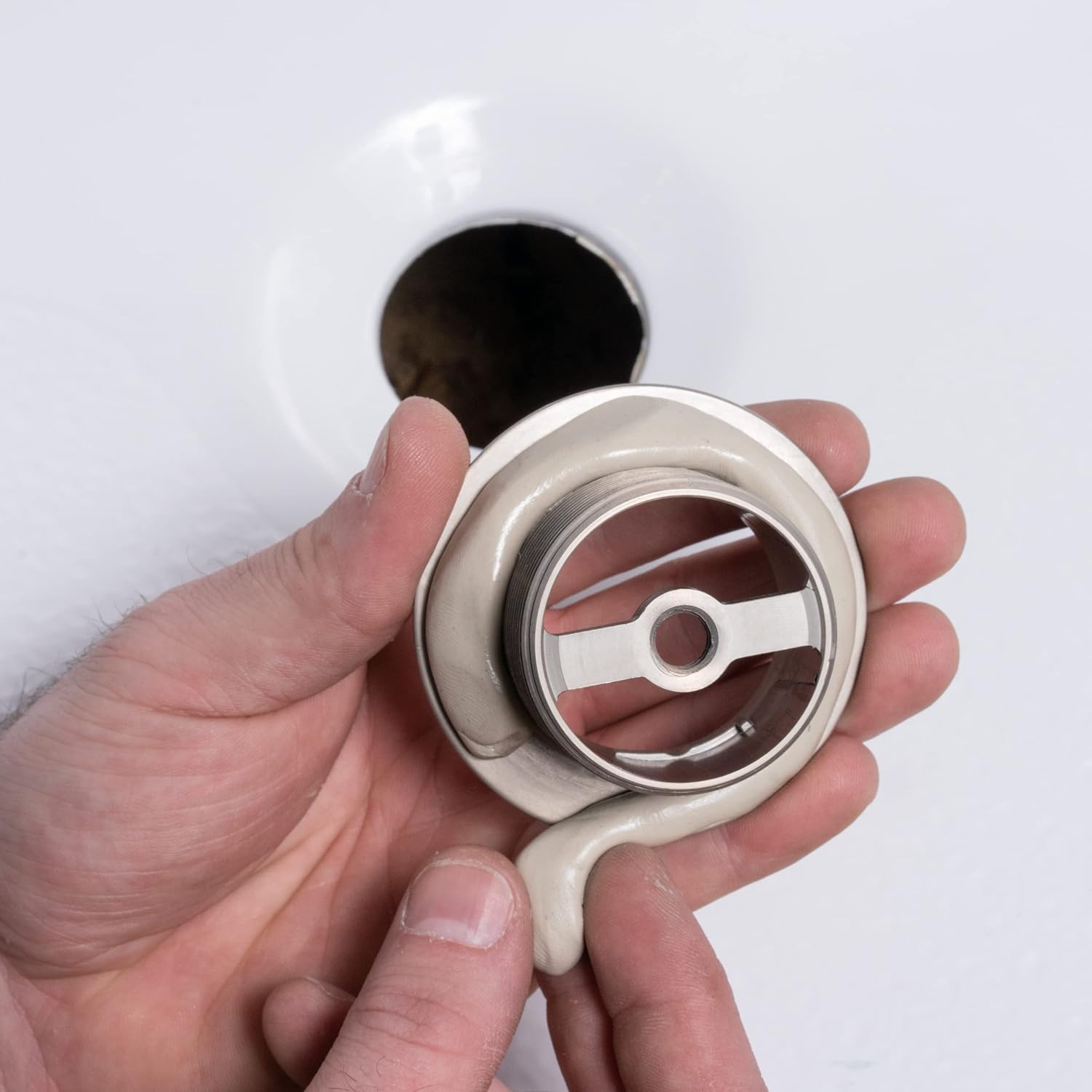 Gray and white plastic plumbers putty container held in hand with metal applicator tool visible inside.