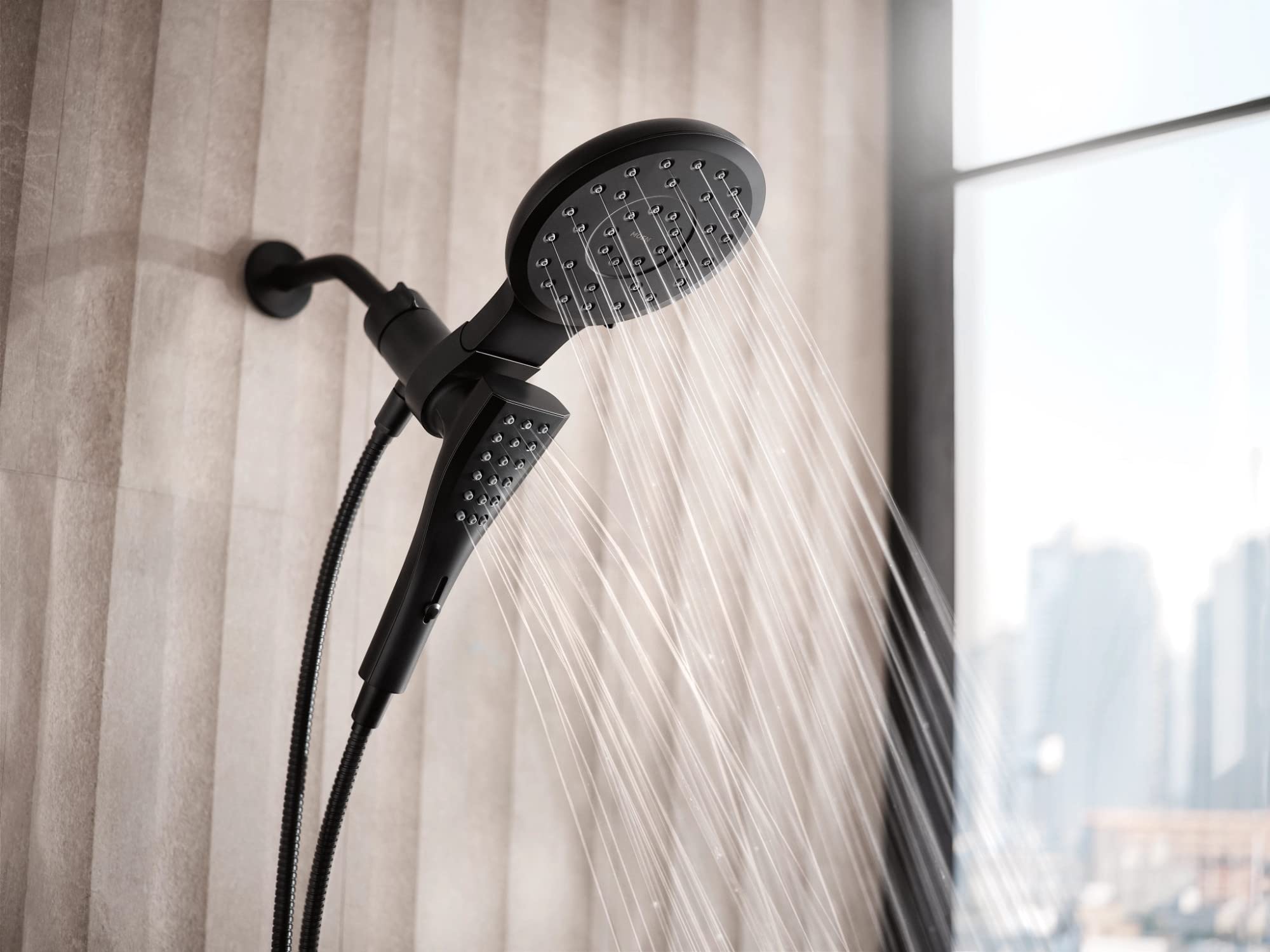 Matte black dual shower head combo with overhead circular head and handheld wand connected by hose, mounted on wall tile.