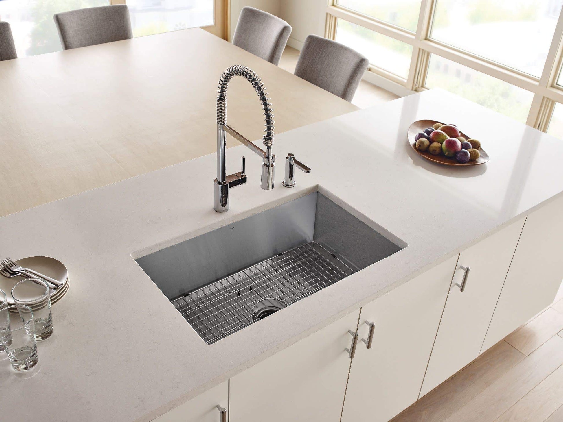 Stainless steel undermount kitchen sink installed in white countertop with grid bottom and faucet.