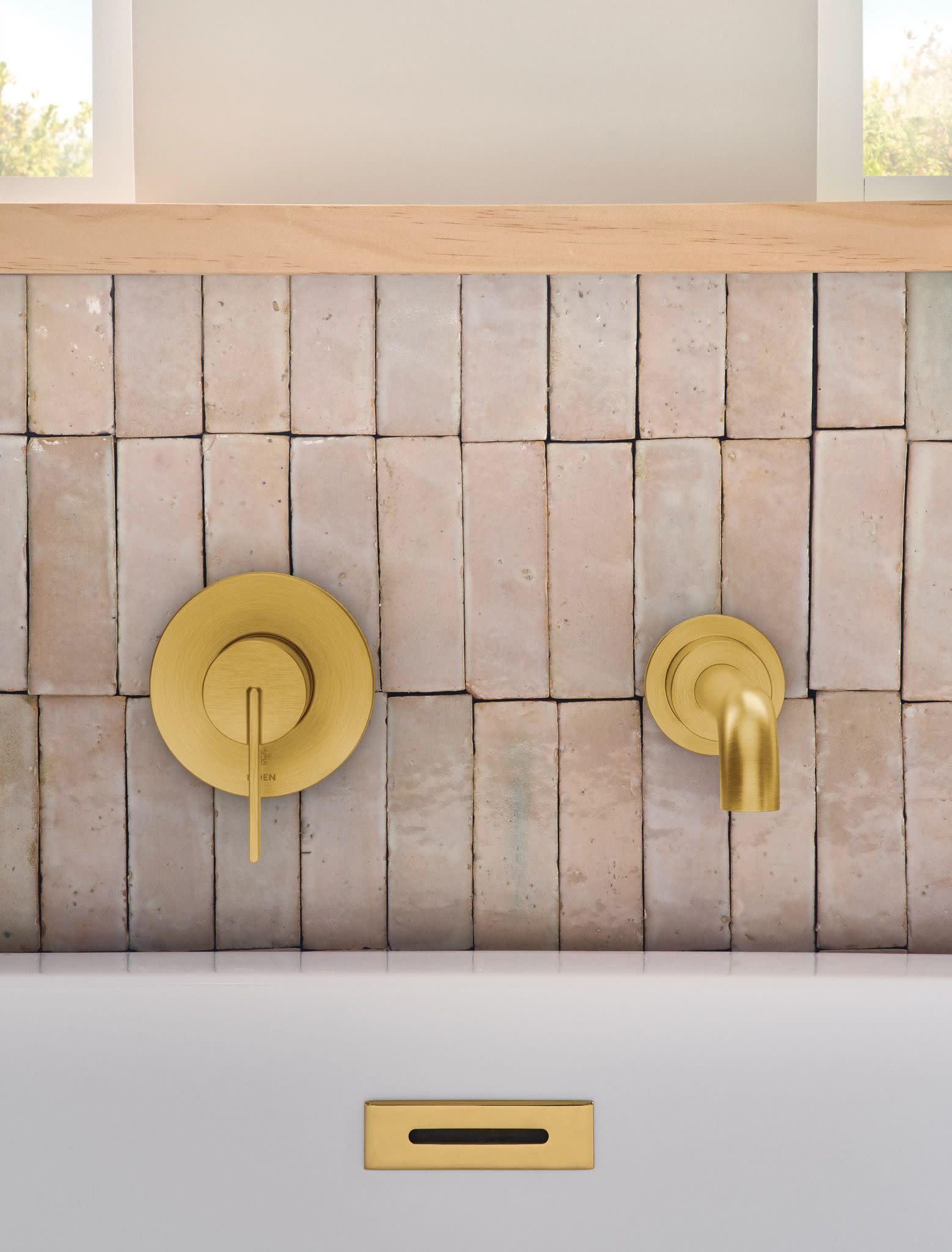 Brushed gold wall-mount tub faucet with single handle lever and curved spout installed on beige subway tile.
