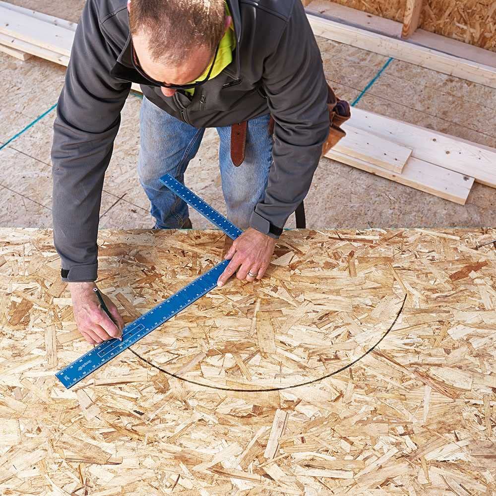 Worker using a blue framing square to mark measurements on plywood during construction.