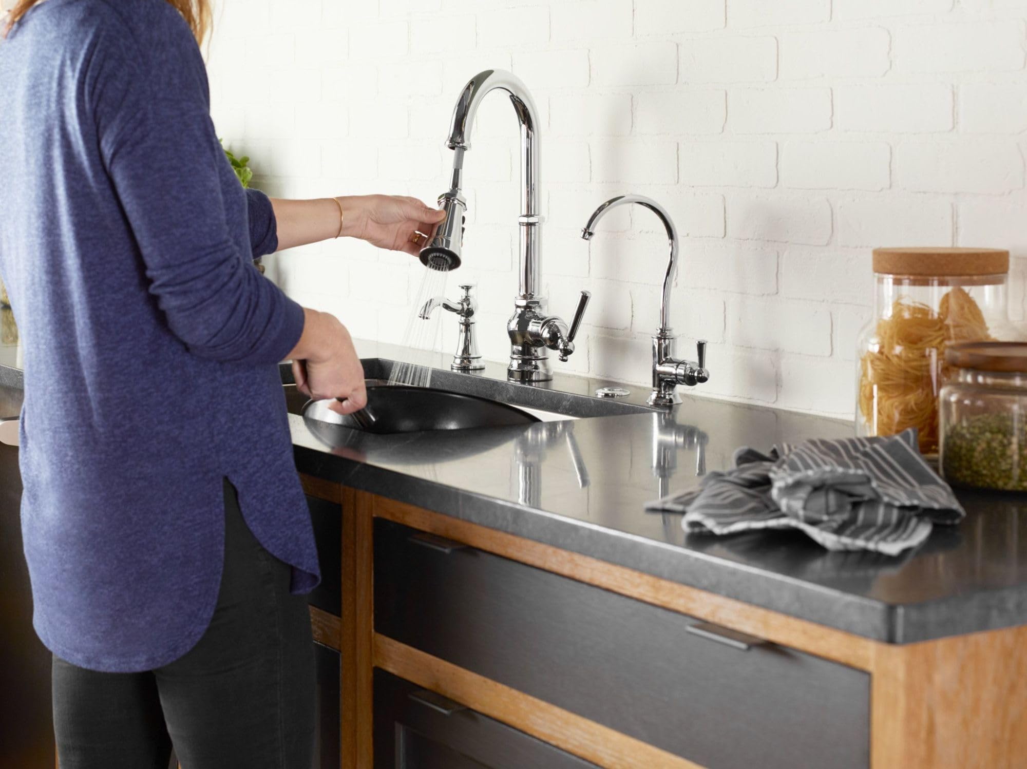 Chrome pulldown kitchen faucet with curved spout mounted on black countertop with white subway tile backsplash.