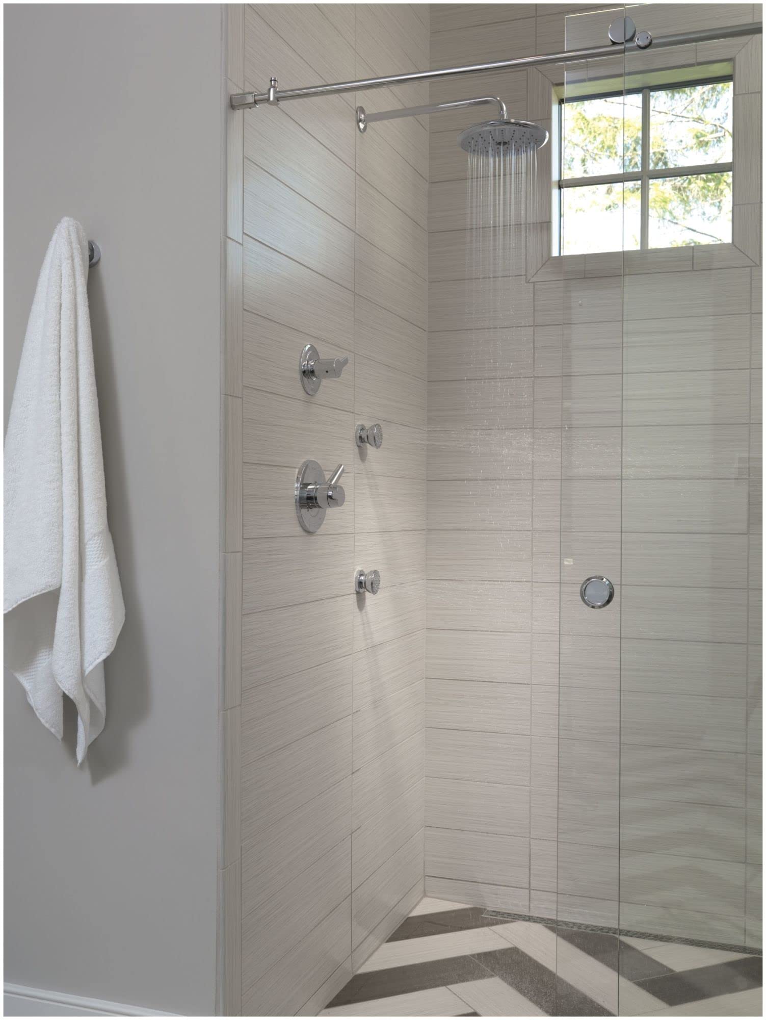 Black stainless steel shower flange with matching valve trim installed above tiled shower enclosure with glass door.