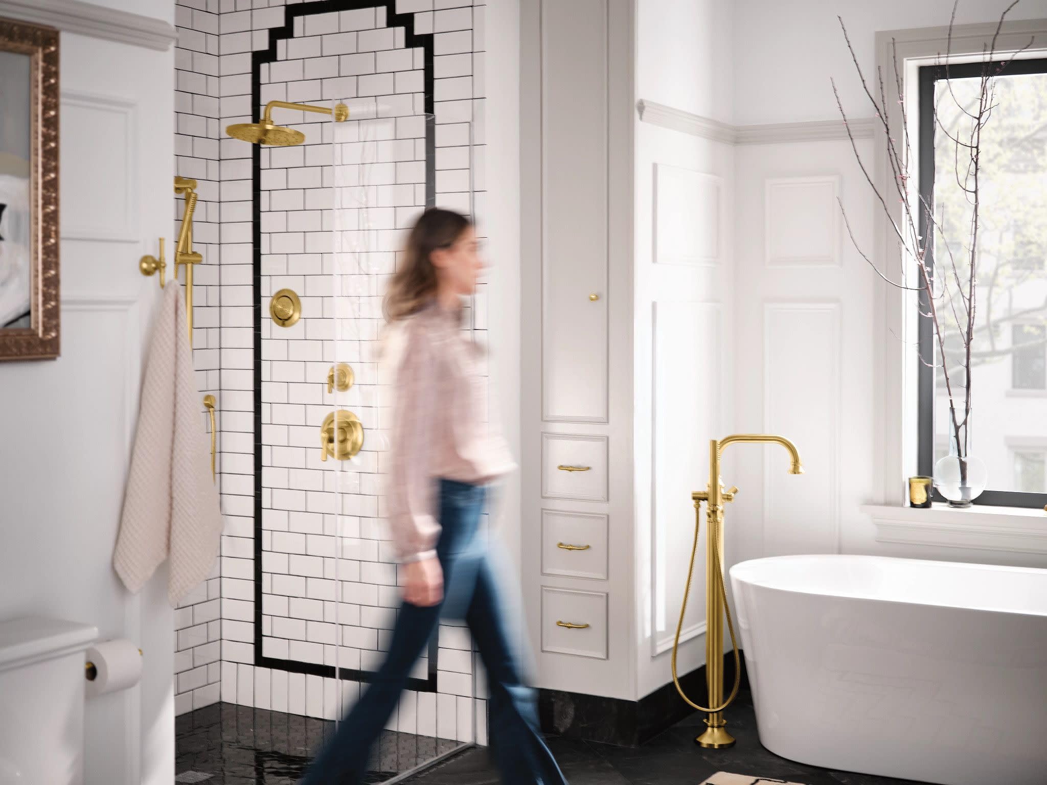 Brushed gold freestanding tub filler with curved spout and handheld shower attachment in modern bathroom setting.