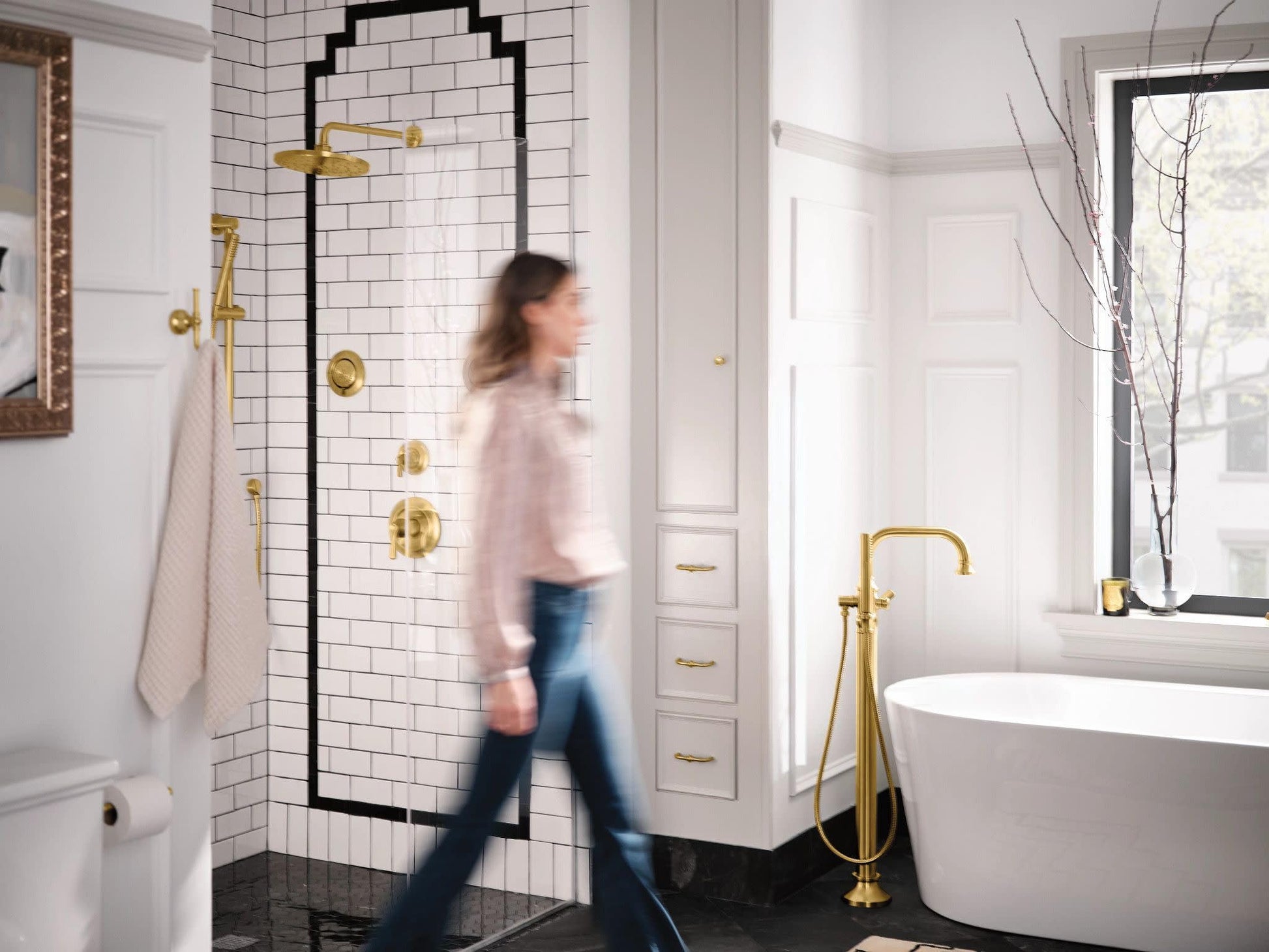Brushed gold shower valve trim with single handle and multiple body jets installed on white subway tile shower wall.